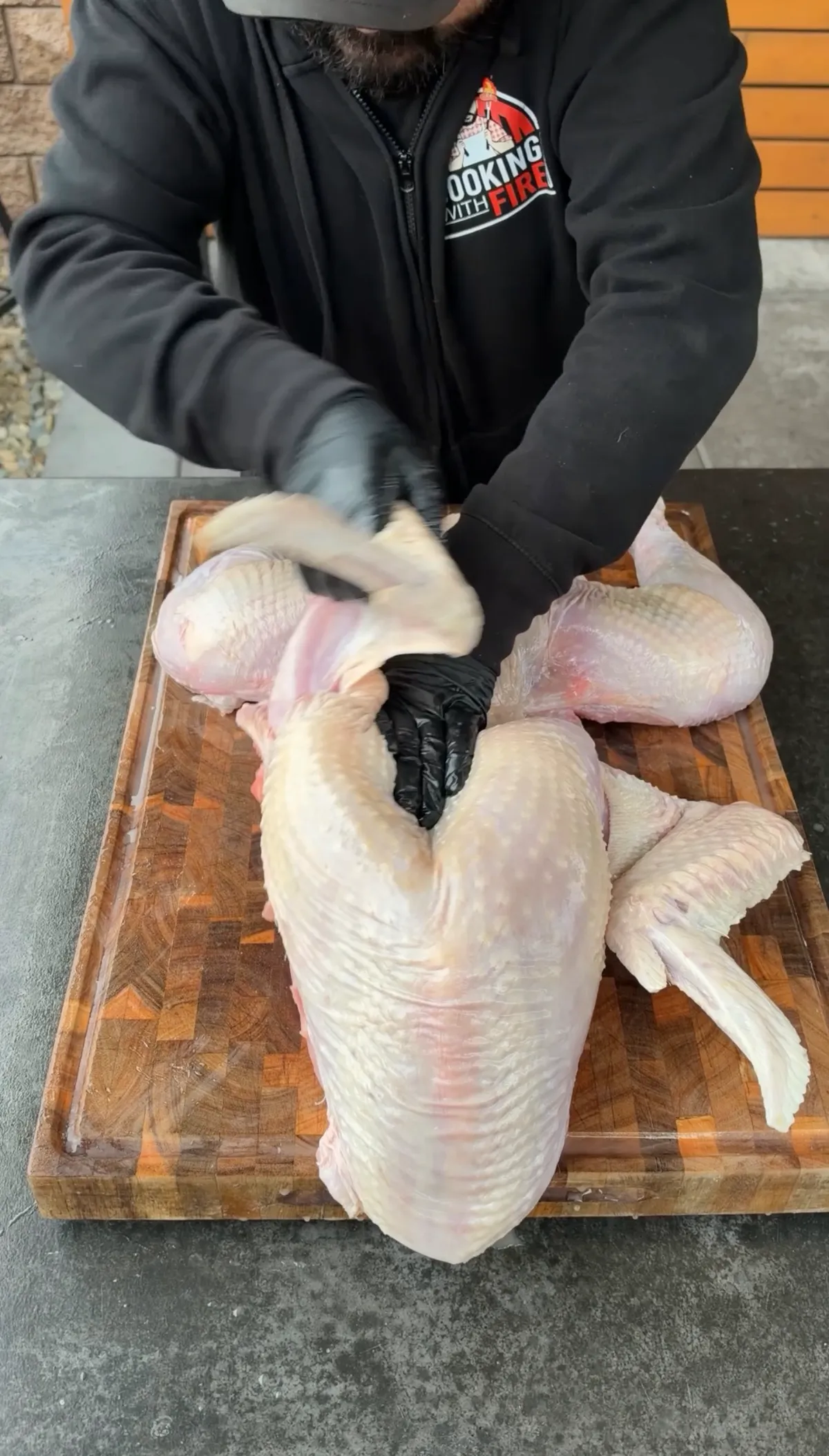 Gloved hands popping turkey leg joints into position on cutting board during frog-style preparation