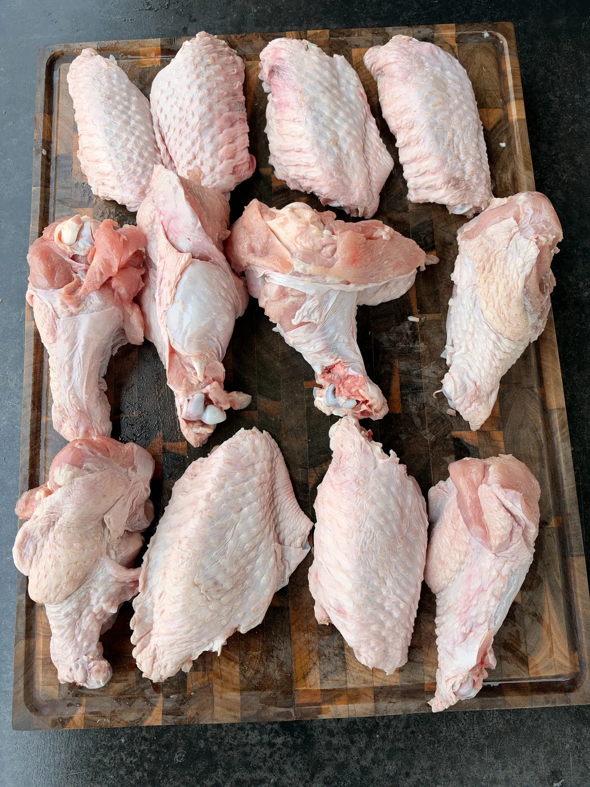 12 raw turkey wing pieces, 6 flats and 6 drums, arranged on a wooden cutting board ready to season