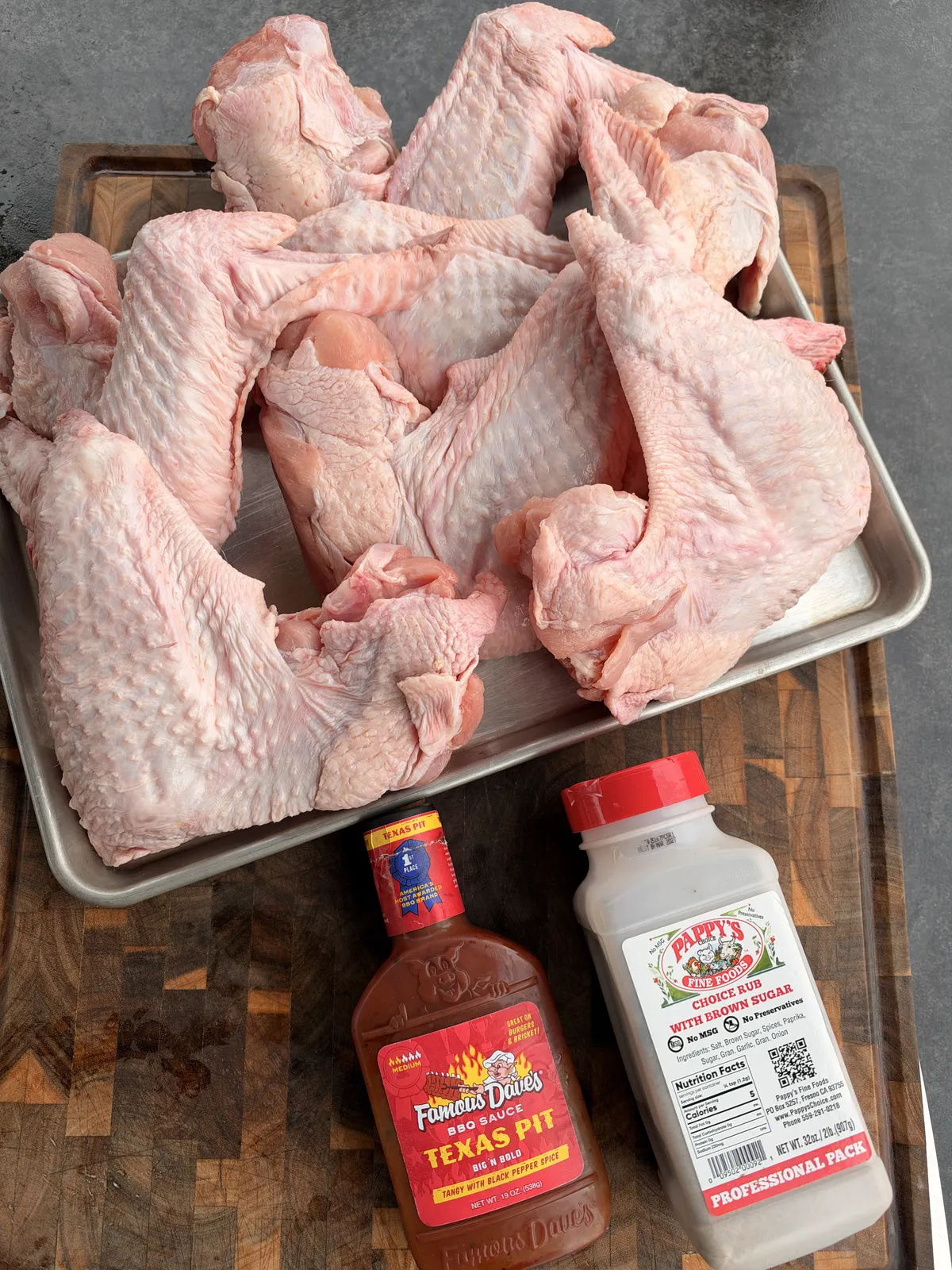 Raw turkey wing pieces on a sheet pan with Pappy's Choice Rub and Famous Dave's Texas Pit BBQ sauce