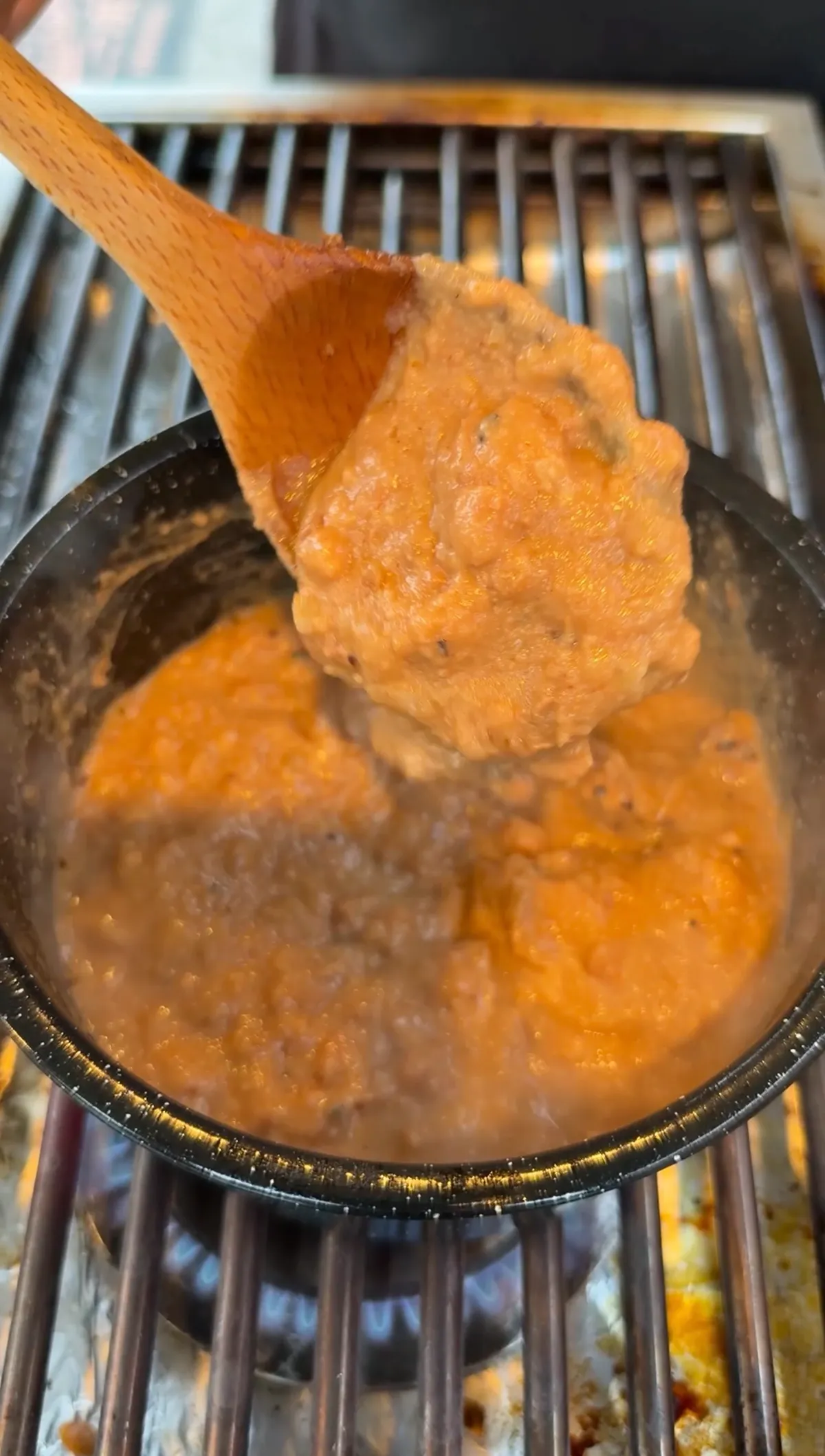 Creamy refried beans with sautéed sweet onion stirred with a wooden spoon in a black skillet on a gas grill