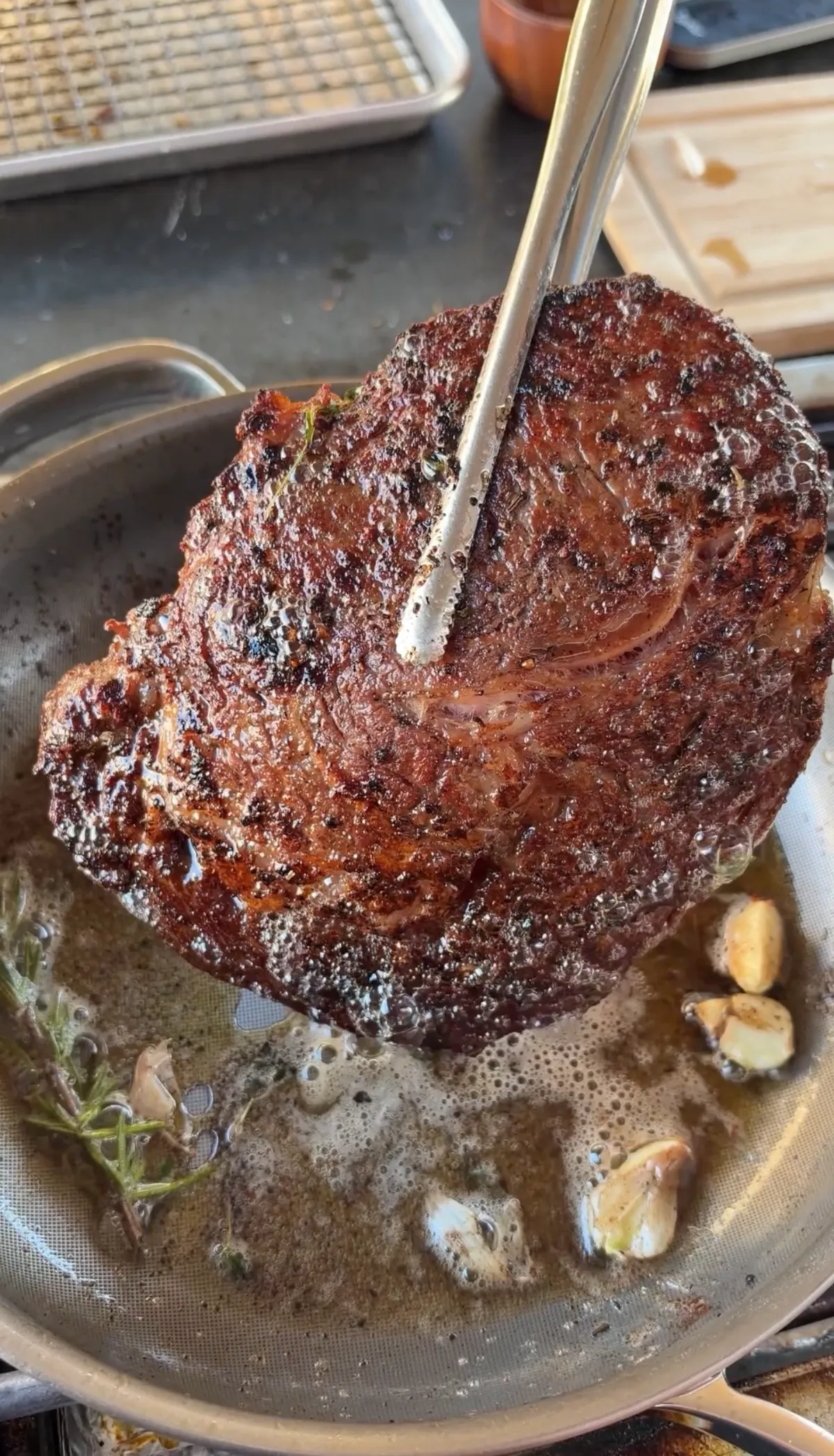 Ribeye steak held upright with tongs over a pan of foamy garlic herb butter with rosemary and thyme