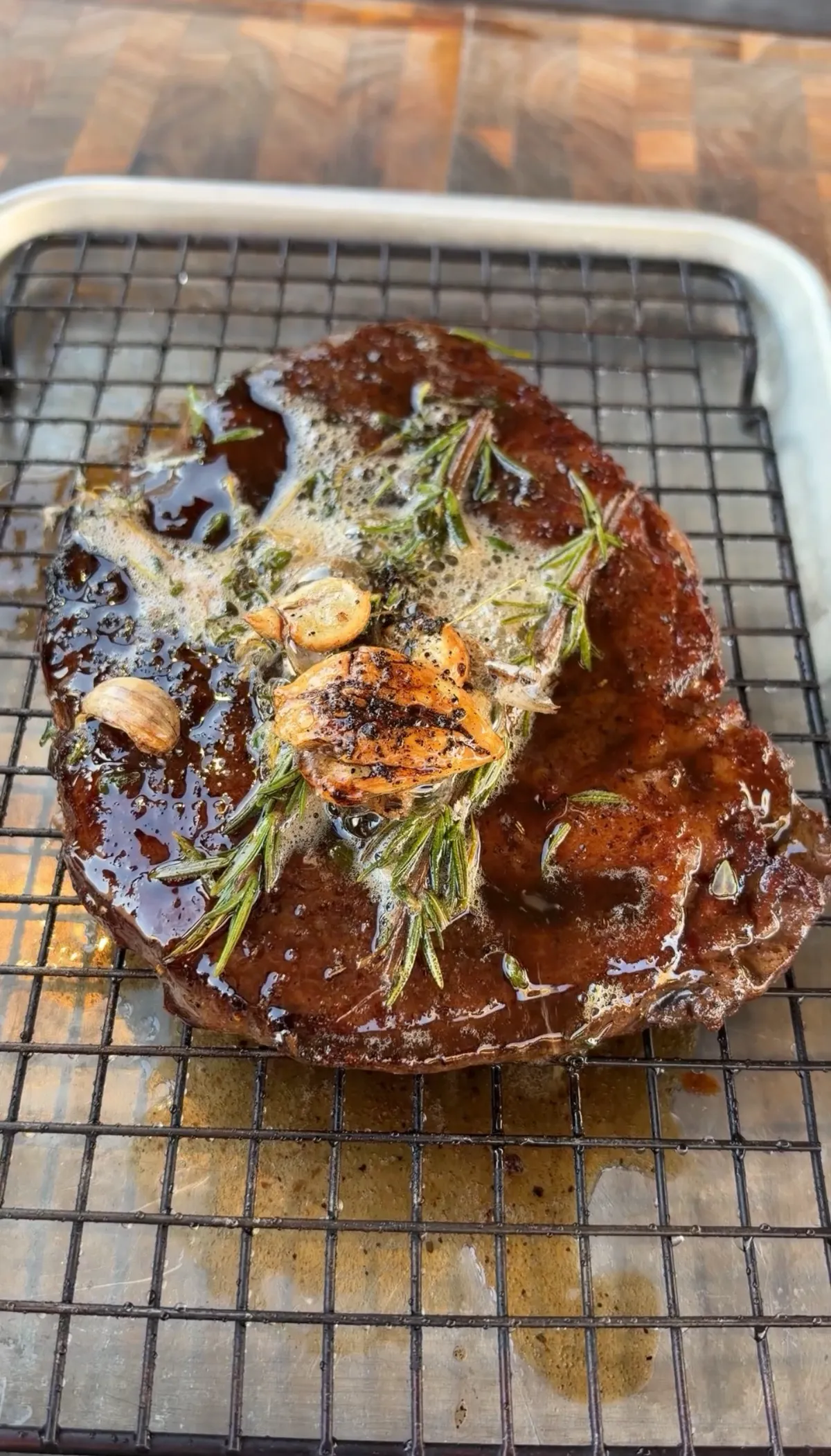 Seared ribeye resting on a wire rack, topped with smashed garlic cloves, rosemary, and glossy garlic herb butter