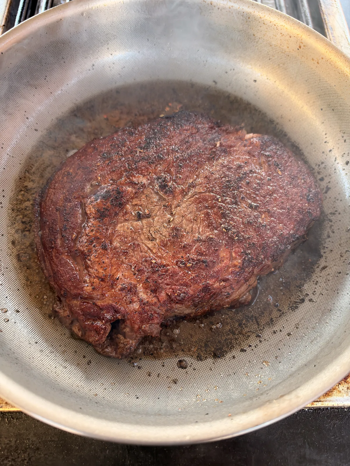 Ribeye steak developing a deep golden-brown crust while searing in a stainless steel pan