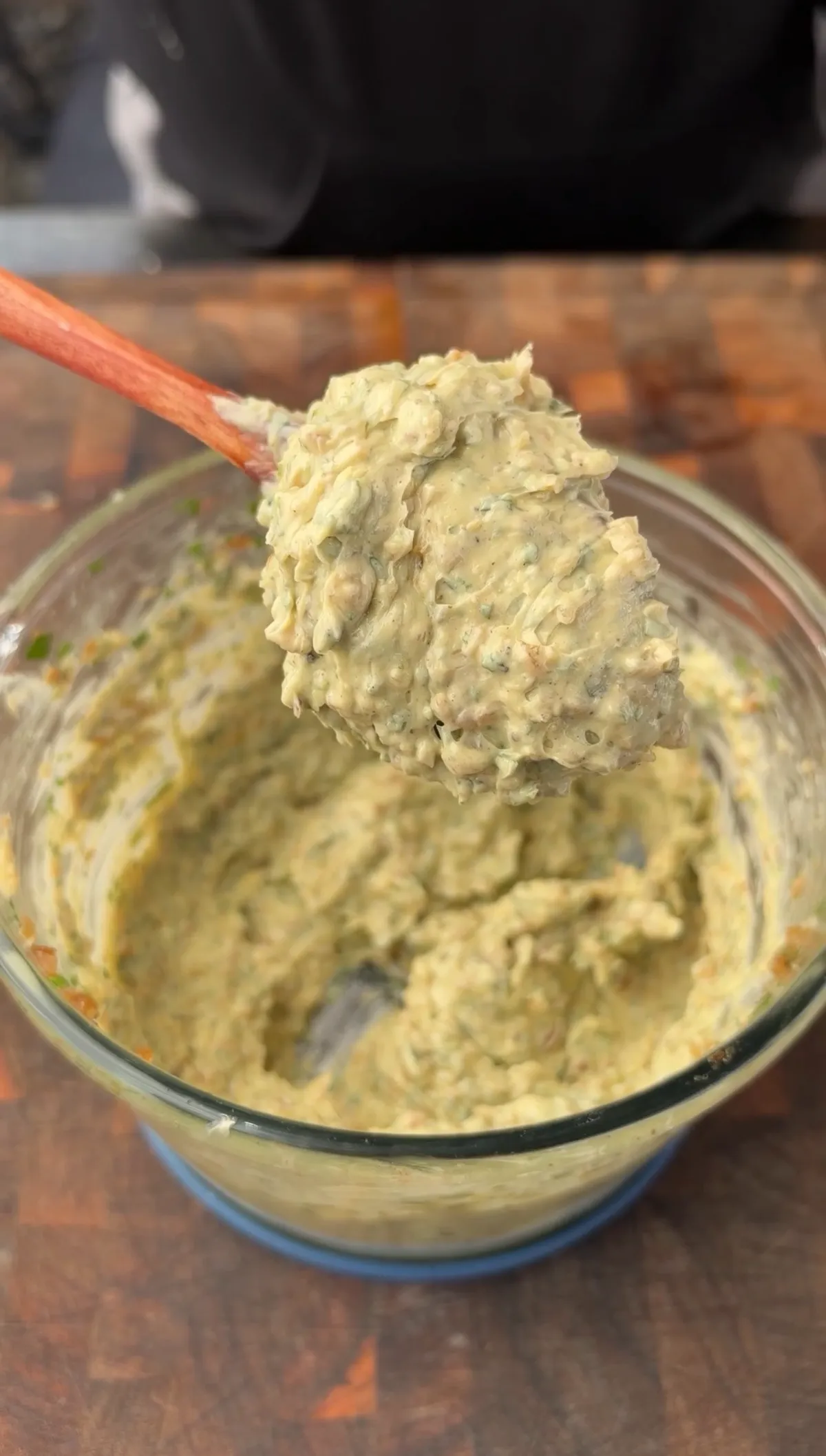 Roasted garlic and onion compound butter with fresh herbs in a glass bowl, lifted with a wooden spoon