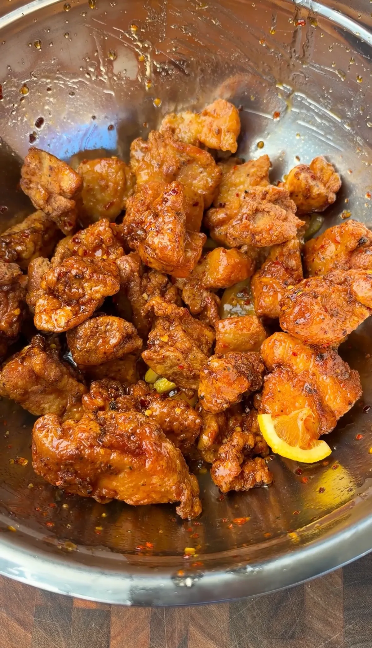 Crispy fried chicken thigh nuggets tossed in hot honey chili oil lemon pepper sauce in a stainless steel bowl