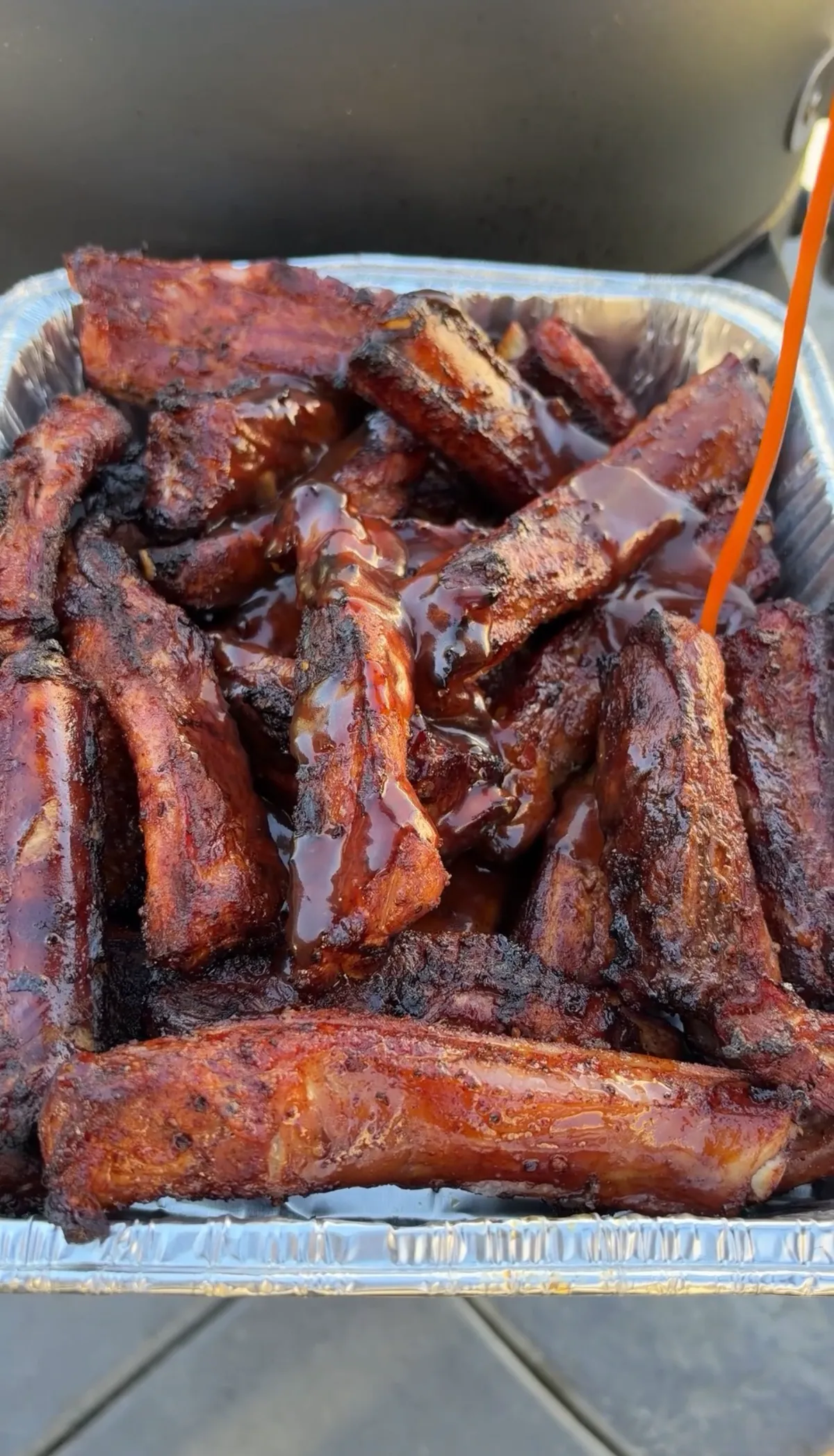 Sticky smoked St. Louis-style party ribs piled high in a foil tray, glazed with shiny barbecue sauce