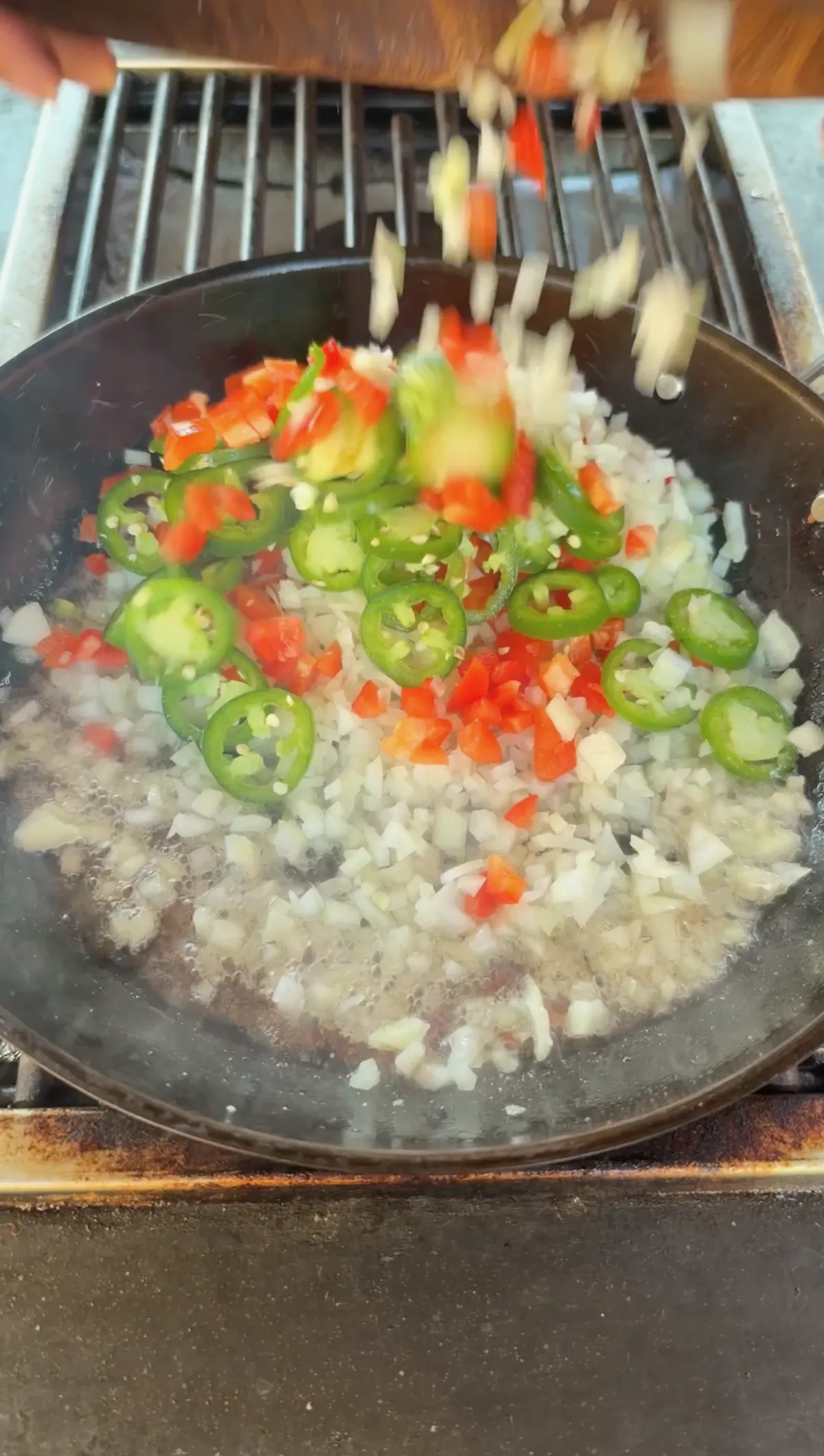 Diced white onion, red bell pepper, and sliced jalapeño rounds being sautéed in a dark skillet