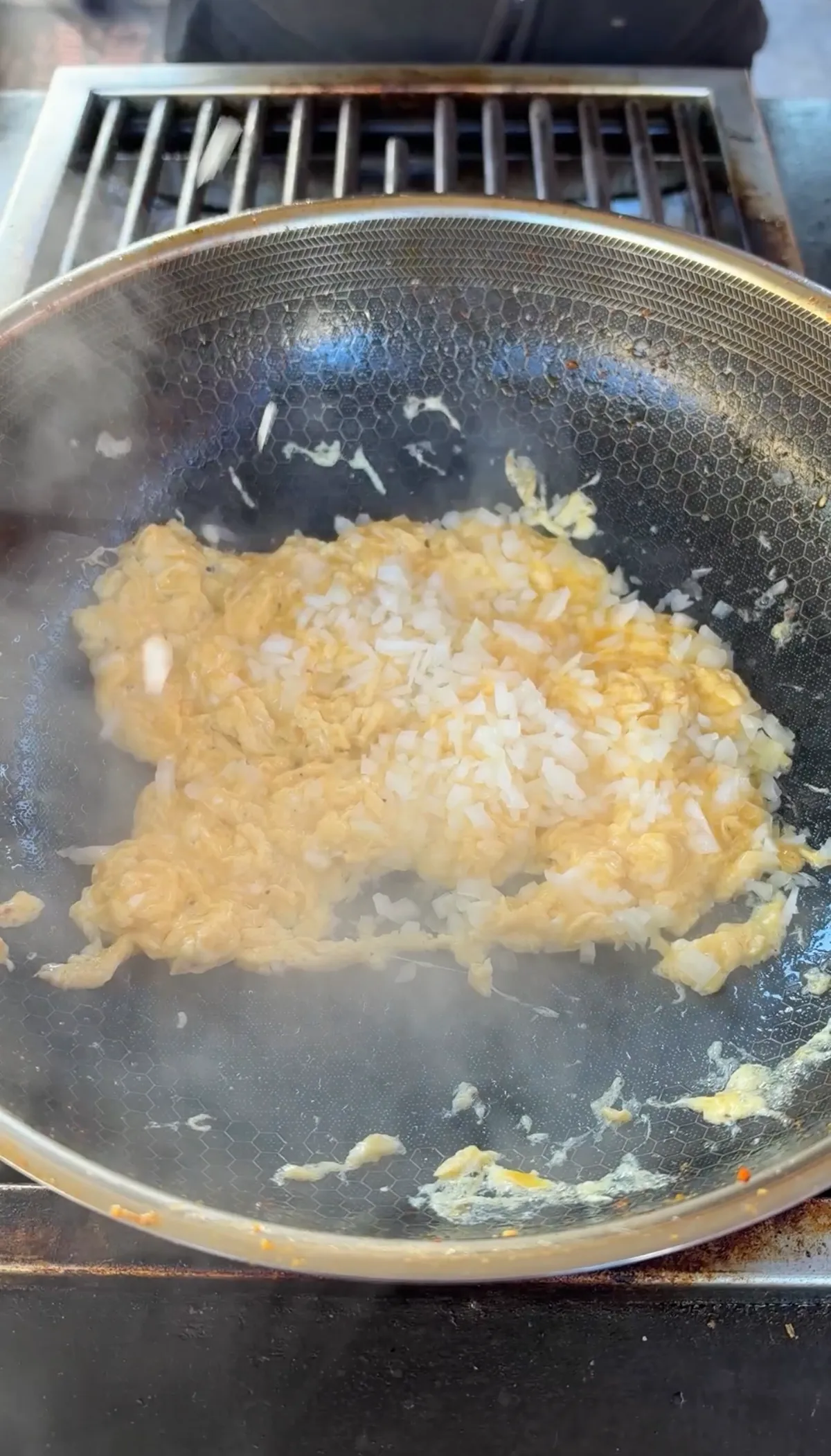 Scrambled eggs and diced yellow onion stir-frying together in a steaming wok over high heat