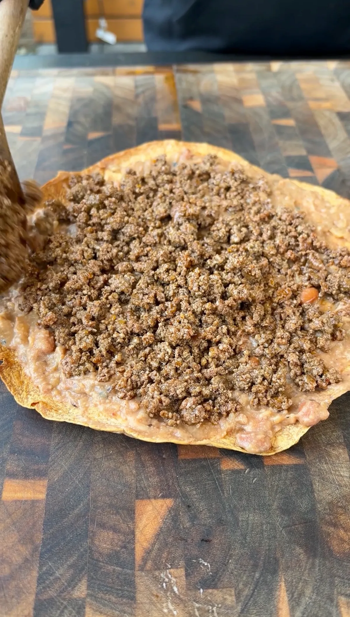 Seasoned ground beef spread over refried beans on a crispy flour tortilla during taco bell mexican pizza copycat assembly