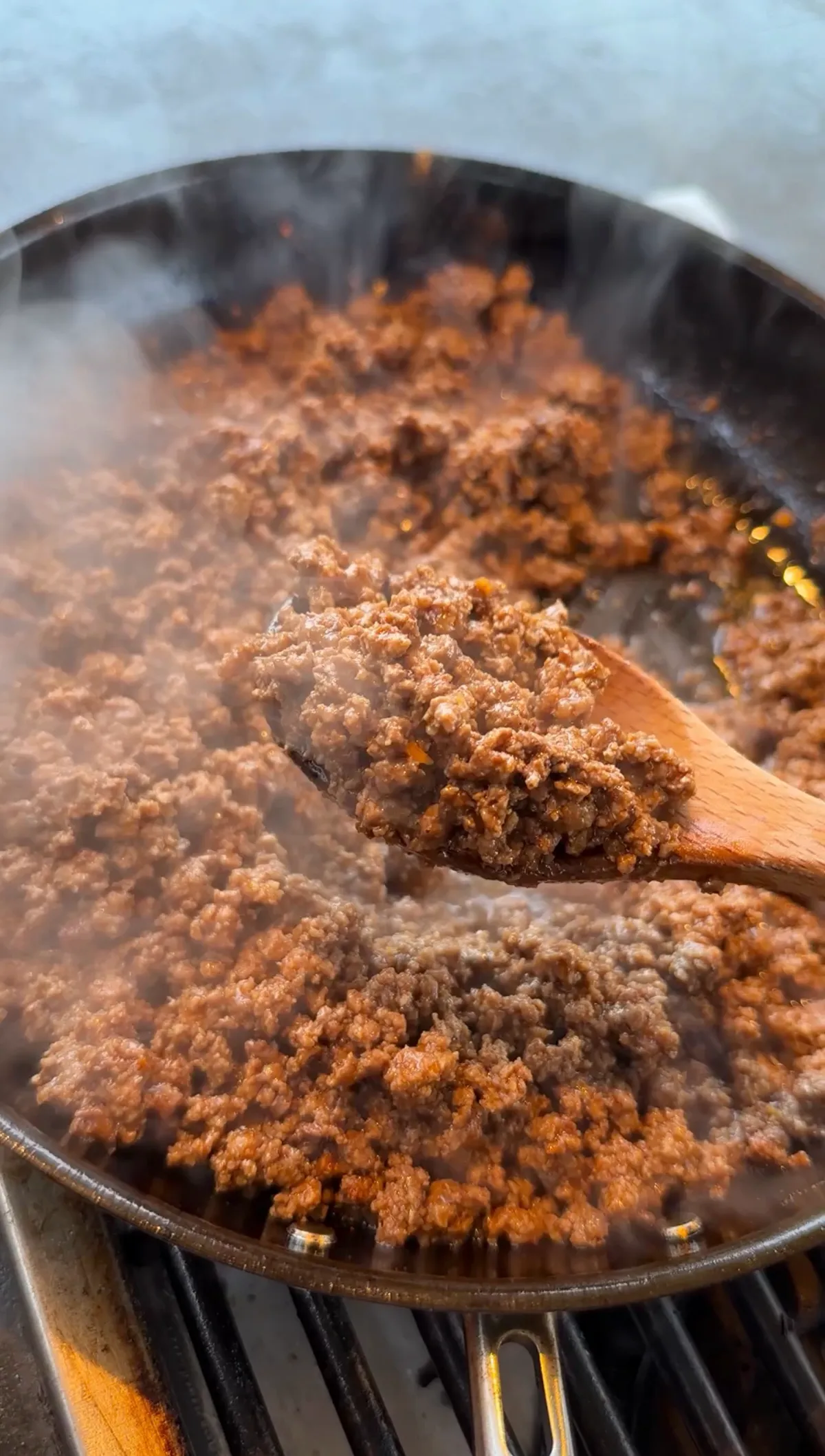 Seasoned ground beef with taco seasoning simmering in a hot skillet, lifted with a wooden spoon