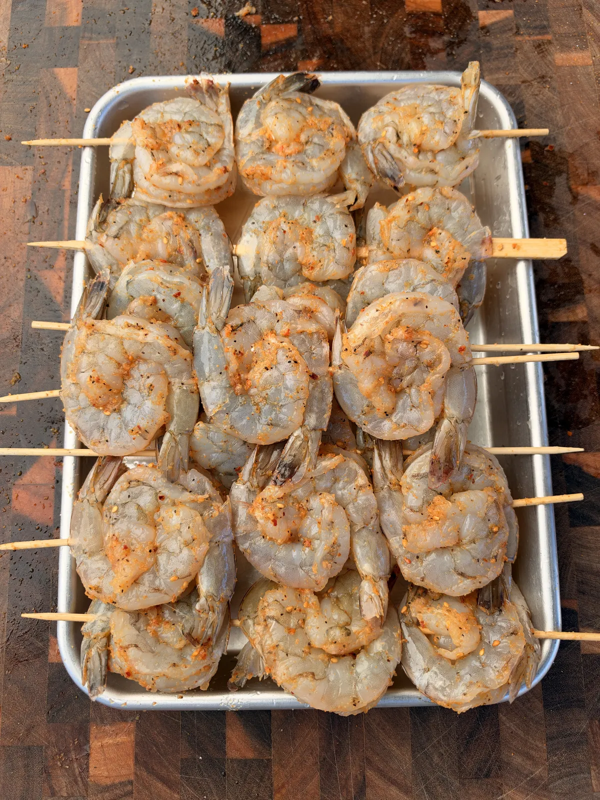 Raw shrimp skewers dusted with seafood seasoning on a metal baking sheet, ready to grill