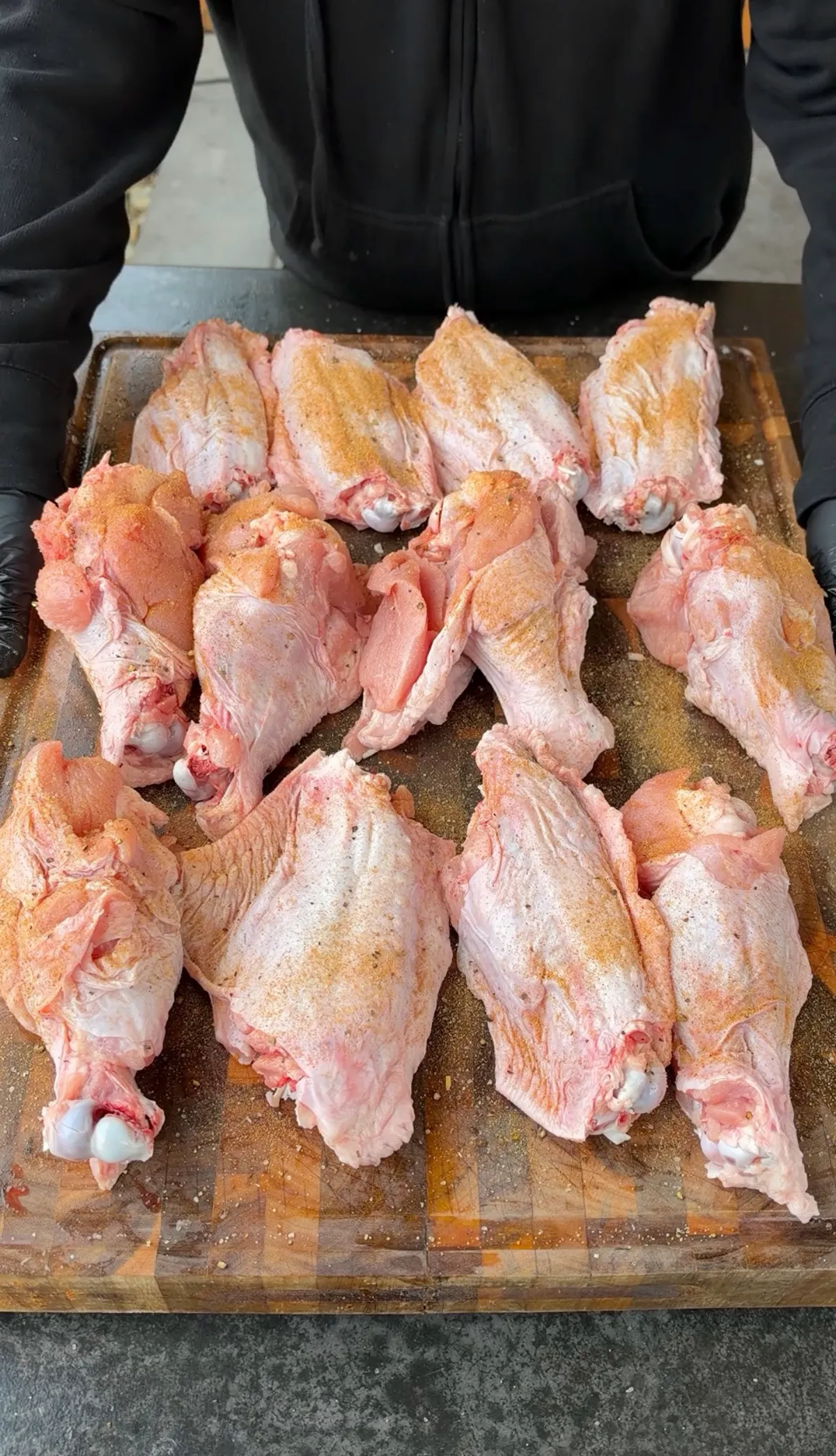 12 raw turkey wing drumettes and flats generously coated in poultry seasoning on a wooden cutting board