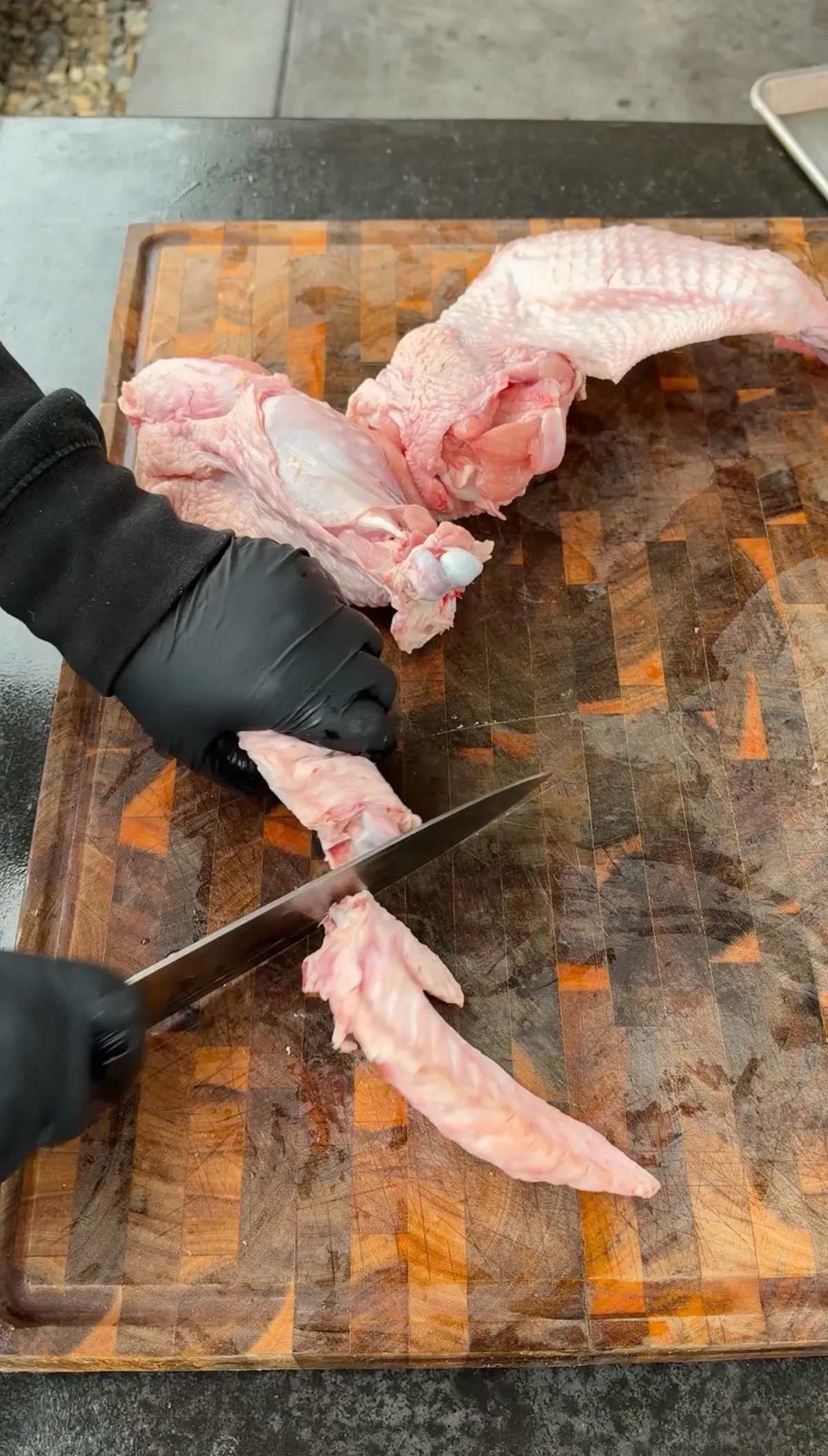Gloved hands using a knife to remove wing tips and separate turkey wing pieces on a wooden cutting board