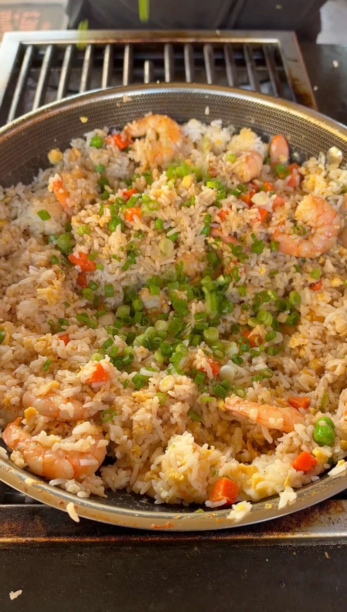 Shrimp fried rice with peas, carrots, scrambled eggs, and sliced green onions in a stainless wok