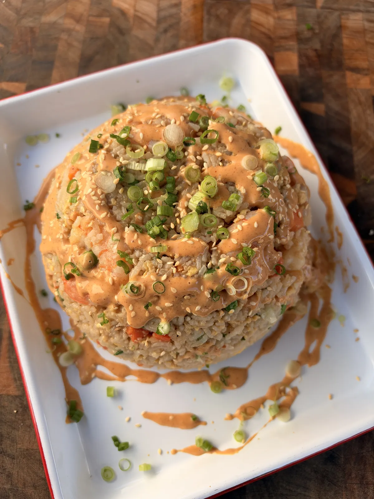 Domed shrimp fried rice topped with yum yum sauce, sesame seeds, and sliced green onions on a white plate