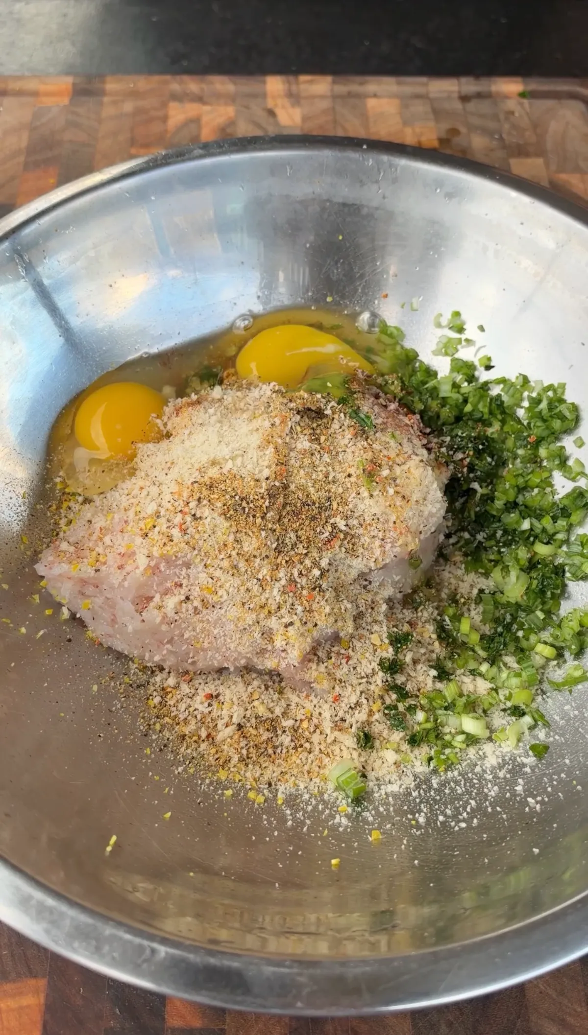 Raw shrimp patty mixture with eggs, panko breadcrumbs, green onions, and seasonings in a stainless steel mixing bowl