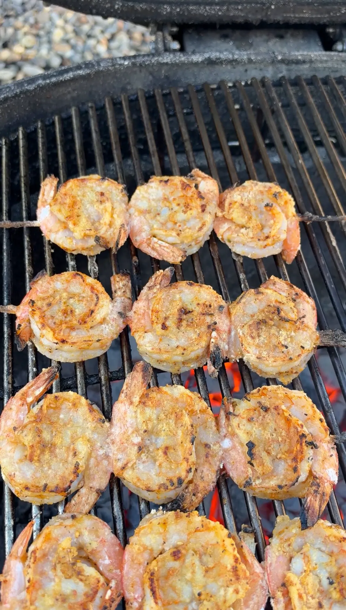 Firecracker shrimp skewers in yin-yang formation grilling over glowing charcoal on cast iron grates