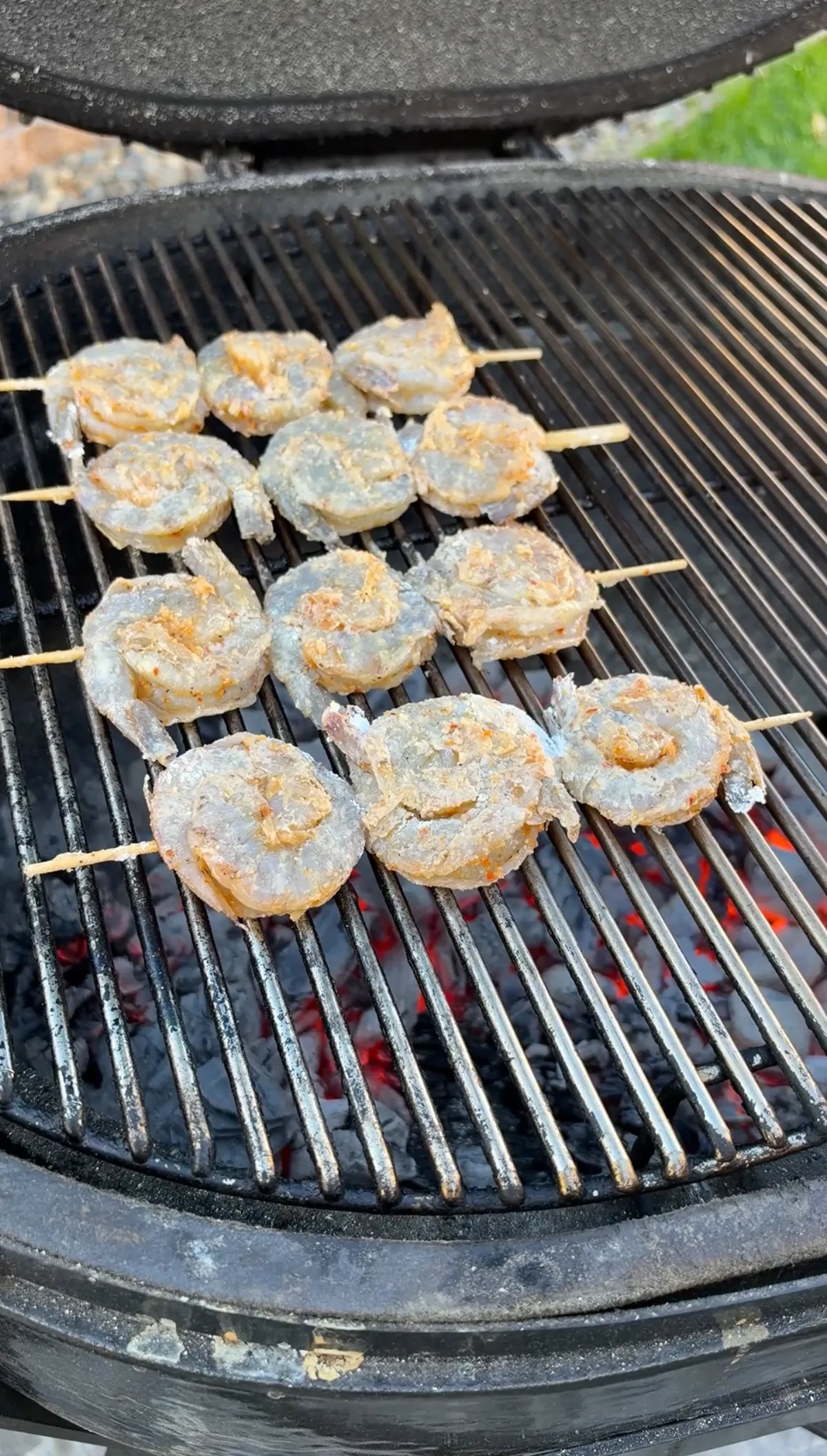 Yin-yang shaped shrimp skewers dusted with cornstarch grilling directly over glowing red charcoal on a kettle grill