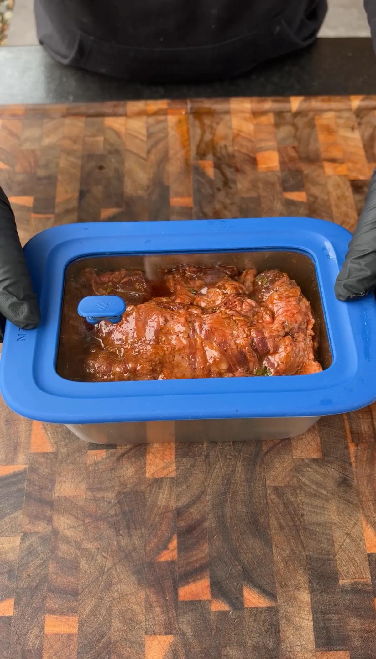 Skirt steak coated in citrus and fajita seasoning marinade in a sealed blue-lidded container on a wood cutting board