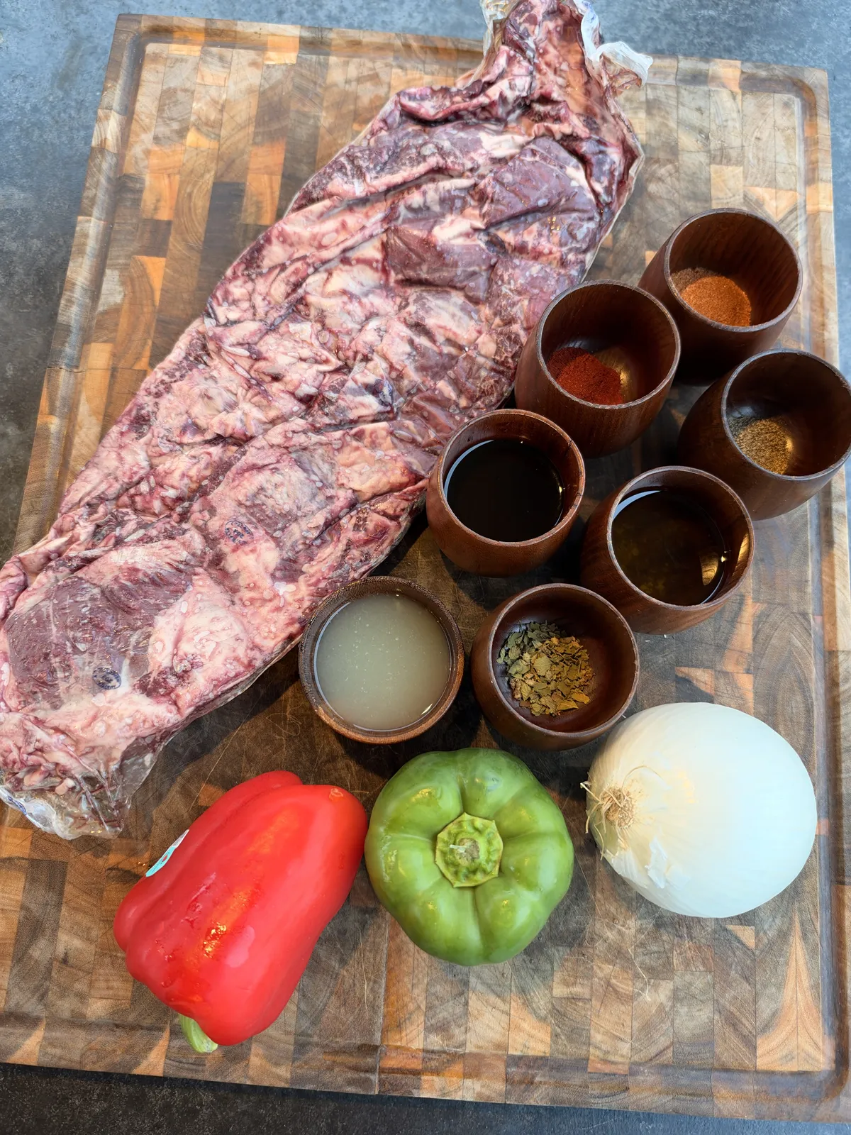 Raw skirt steak with marinade spices, Worcestershire, soy sauce, lime juice, bell peppers, and white onion on a wooden board