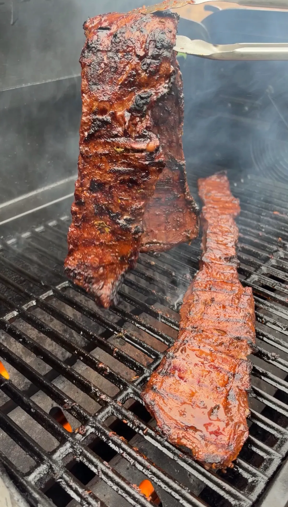 Skirt steak held upright with tongs over hot grill grates, showing deep char and citrus marinade glaze