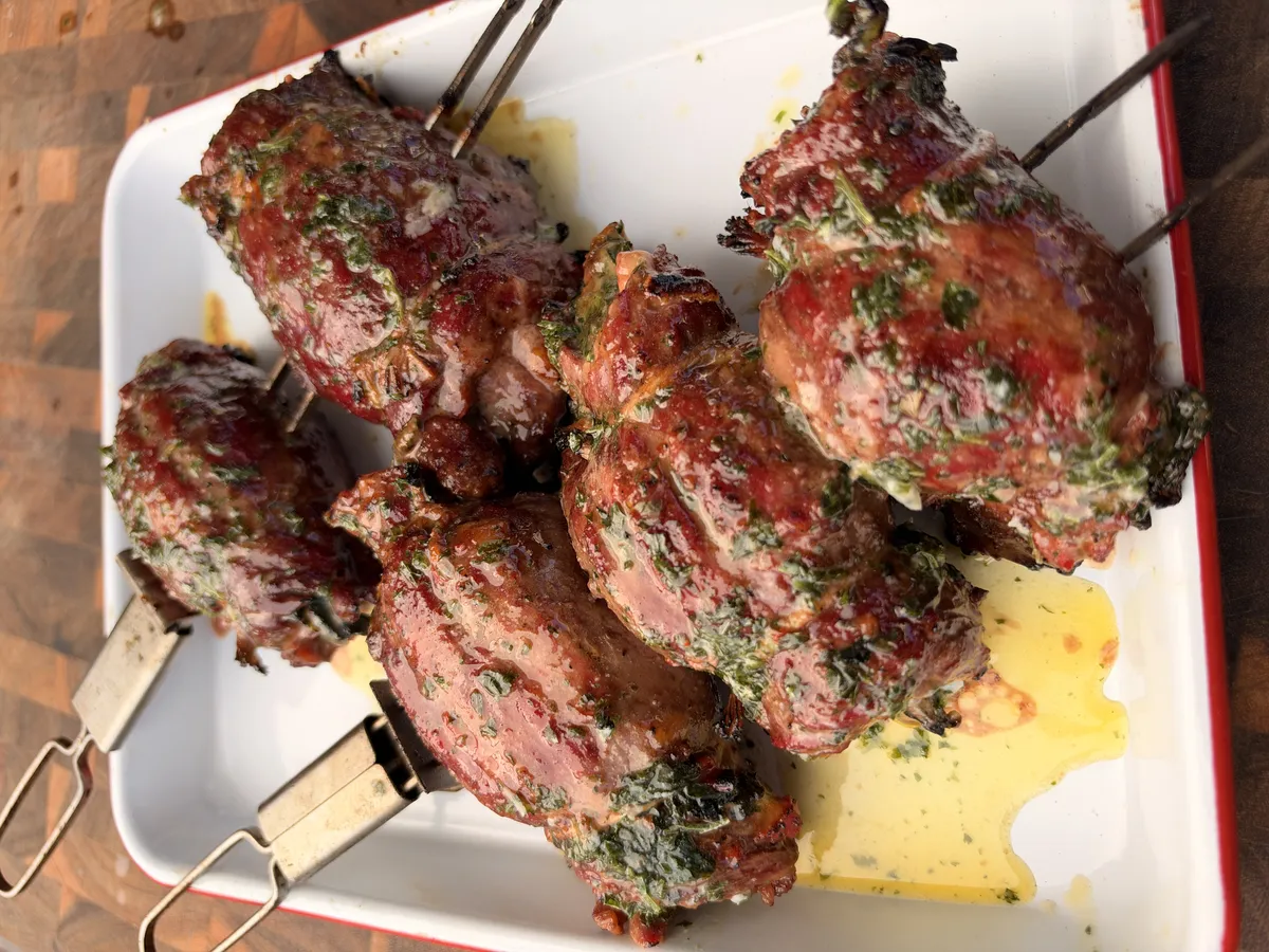 Grilled skirt steak stuffed pinwheels on skewers basted with garlic-parsley butter on a white platter