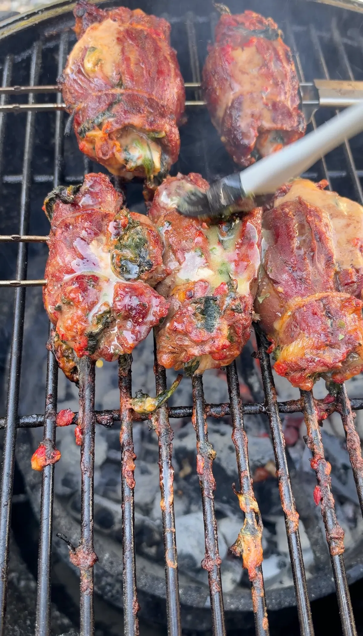 Skirt steak stuffed pinwheels grilling over charcoal, being basted with garlic-parsley butter with visible spinach filling