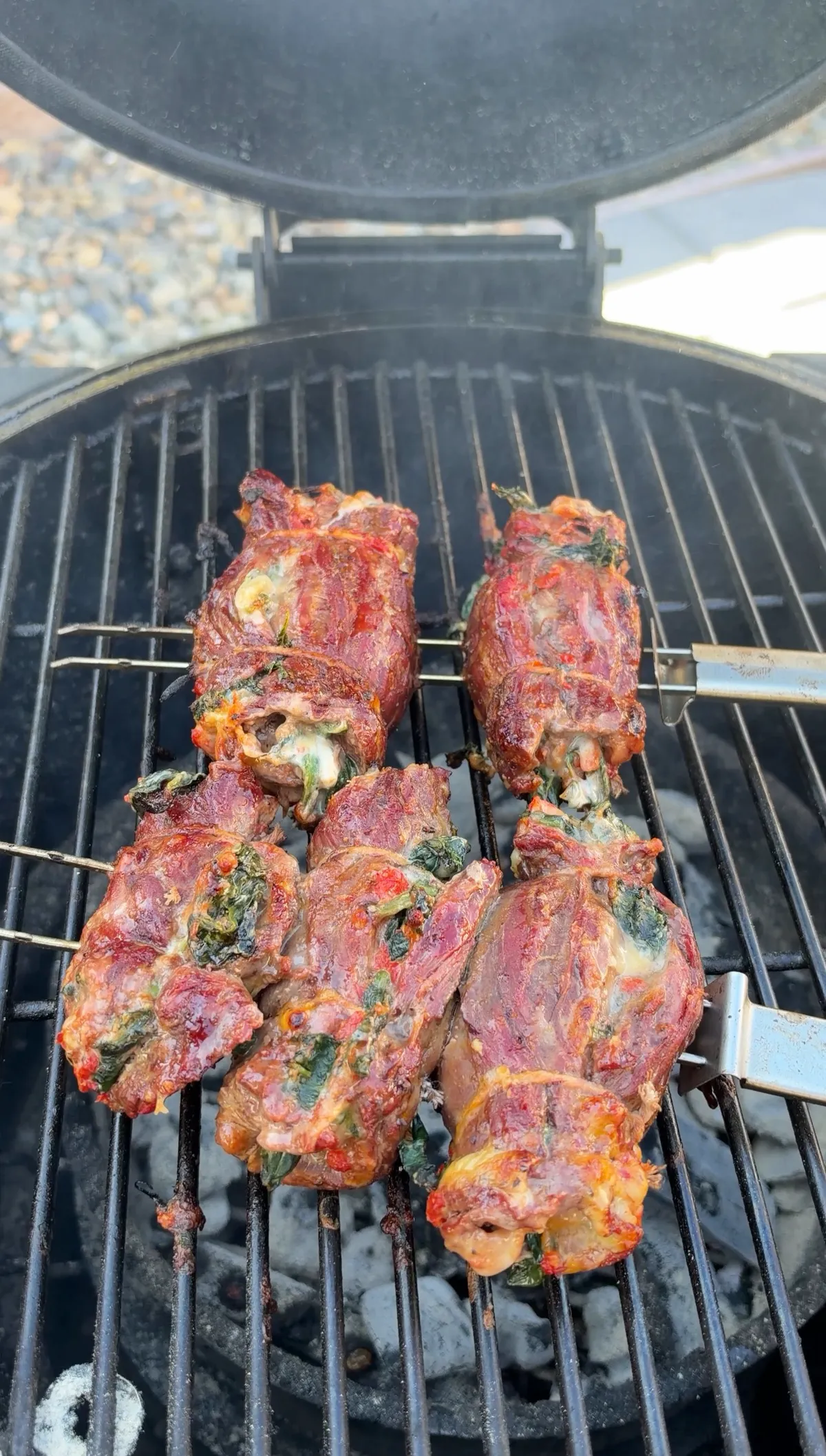 Skirt steak stuffed pinwheels on skewers grilling over charcoal with spinach, roasted red peppers, and Colby Jack filling visible