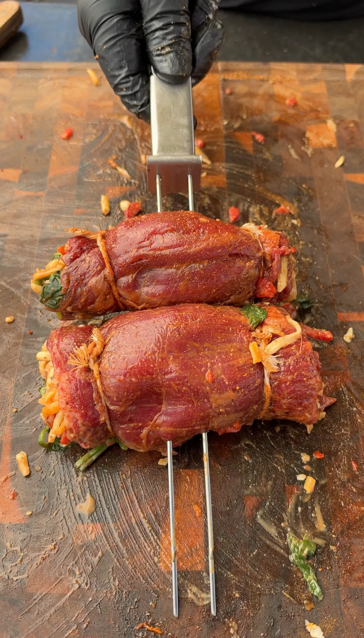 Two skirt steak stuffed pinwheels tied with butcher's twine on skewers, filled with spinach, roasted red bell peppers, and Colby Jack cheese, ready to grill
