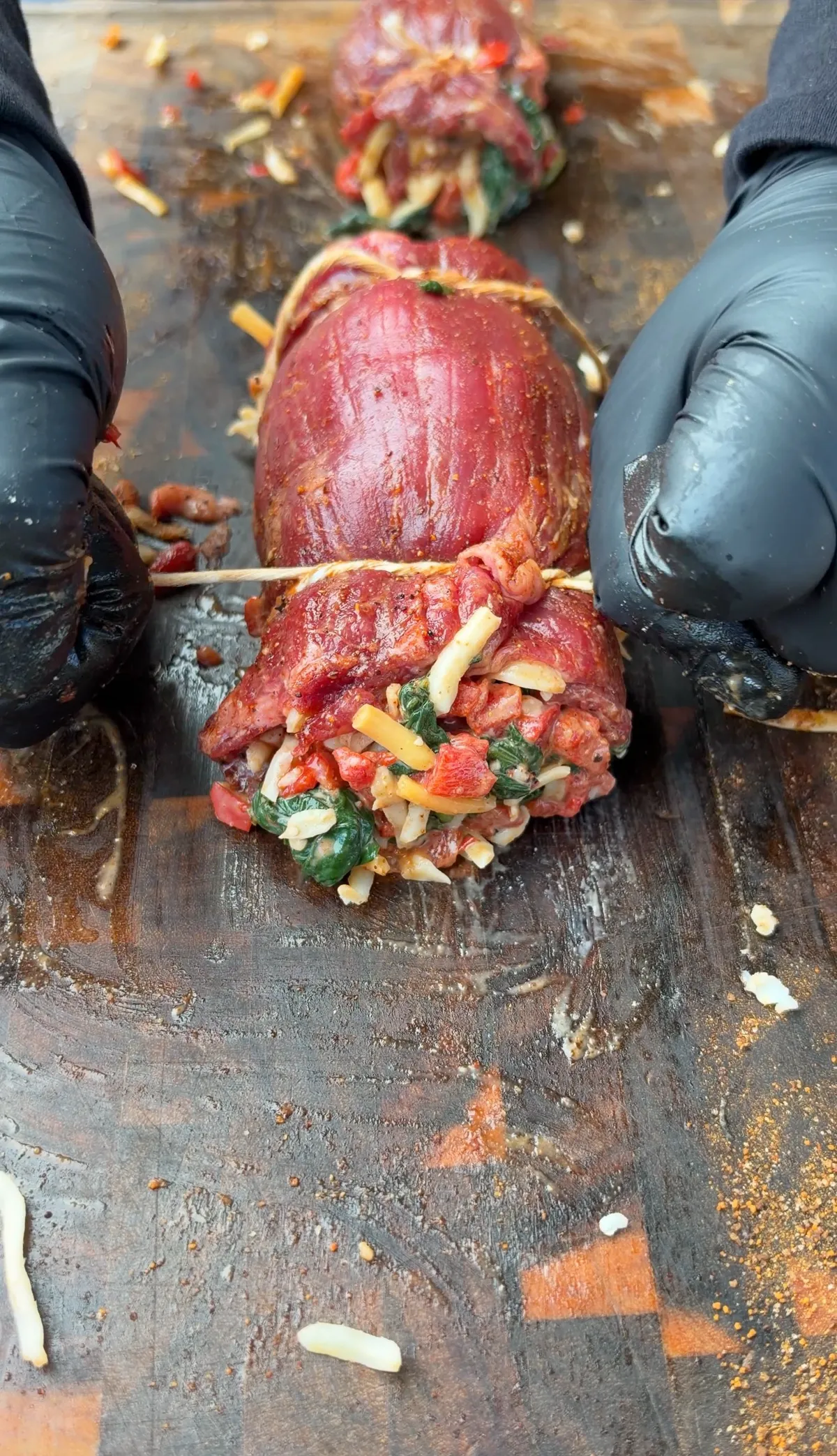 Raw skirt steak pinwheels stuffed with creamy spinach, roasted red bell peppers, and Colby Jack cheese, tied with butcher's twine on a cutting board
