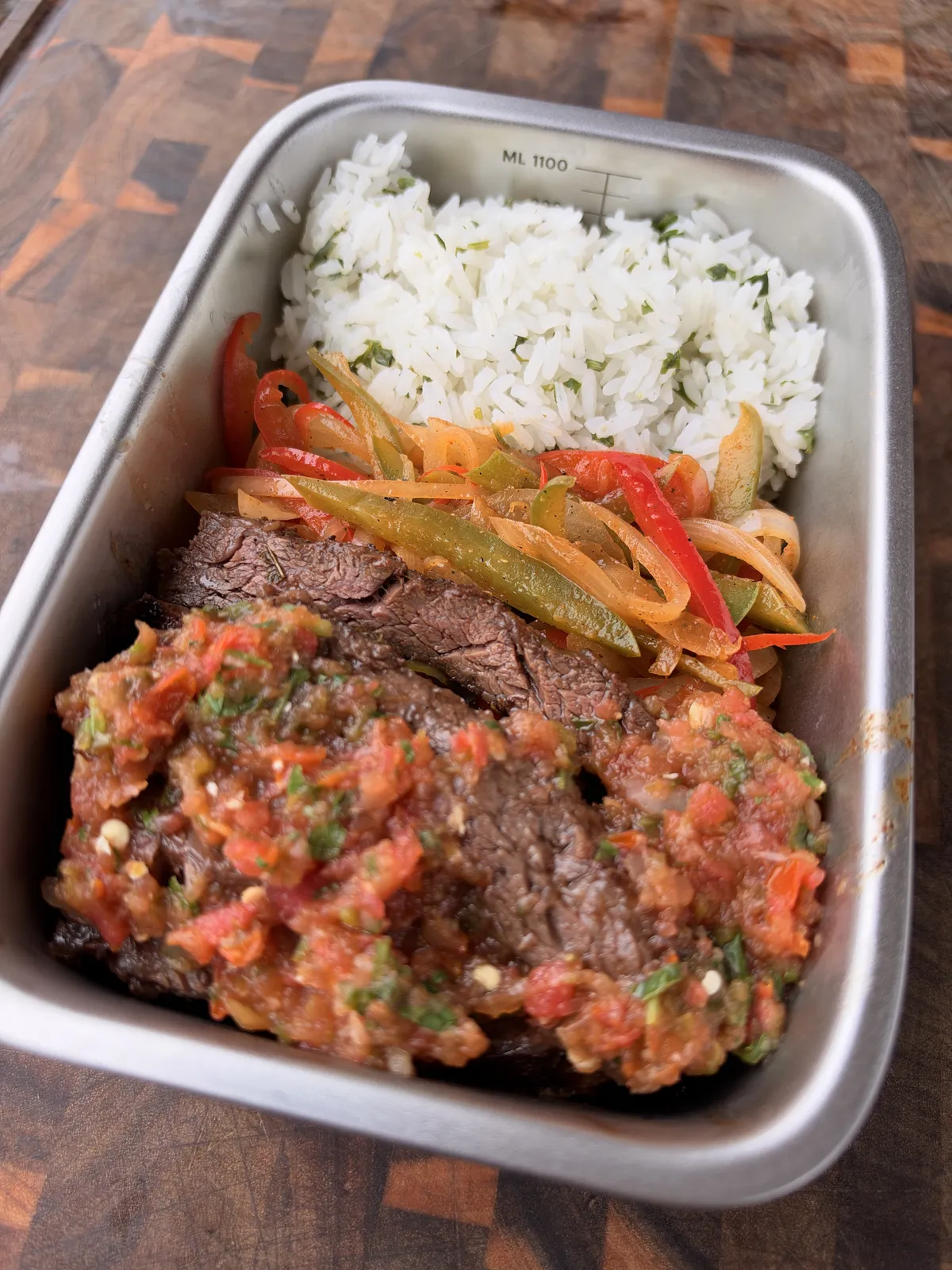 Grilled skirt steak topped with homemade cooked salsa and charred bell peppers and onions, served with cilantro lime rice in a stainless steel meal prep container