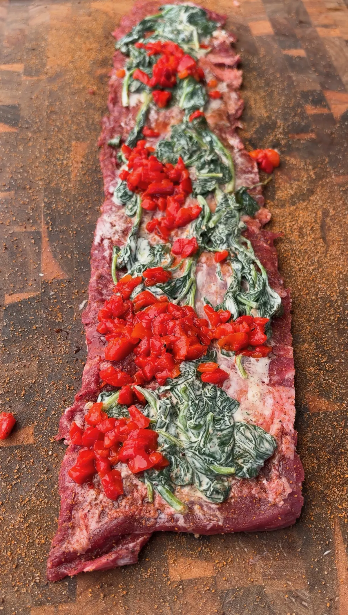 Flattened skirt steak topped with creamy spinach, roasted red bell peppers, and Colby Jack cheese, ready to roll into pinwheels