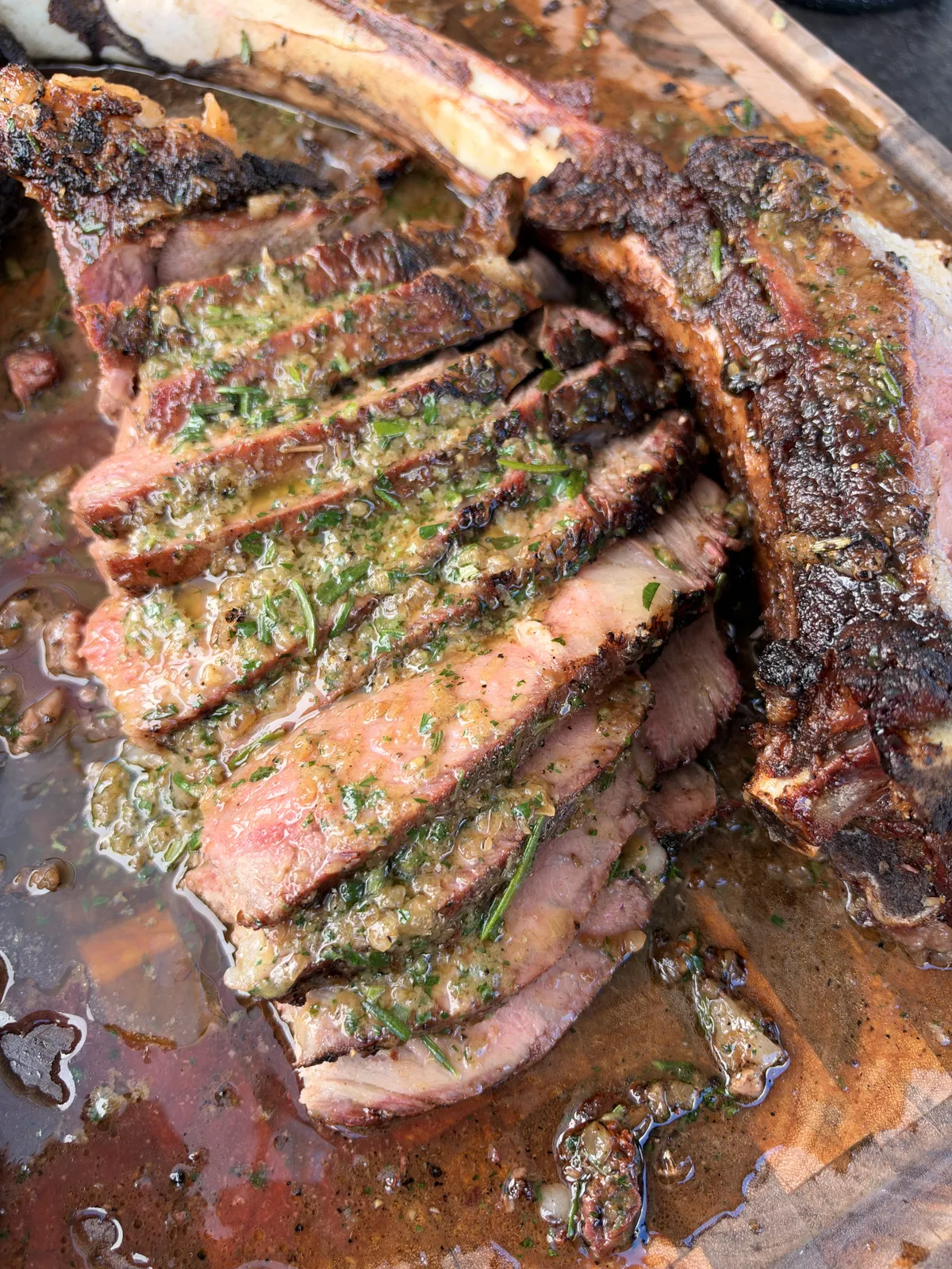 Two-bone prime rib tomahawk sliced against the grain with roasted garlic and onion compound butter melting over each slice on a wooden board