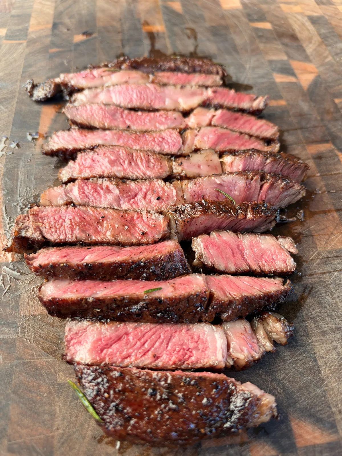 Pan-seared ribeye steak sliced against the grain revealing a medium-rare pink center on a wood cutting board