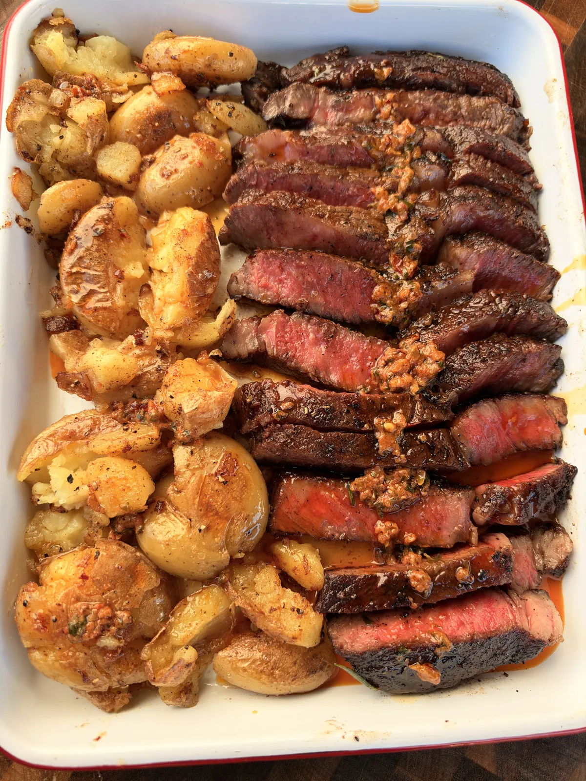 Sliced pan-seared ribeye with garlic herb butter and crispy smashed golden potatoes in a white baking dish