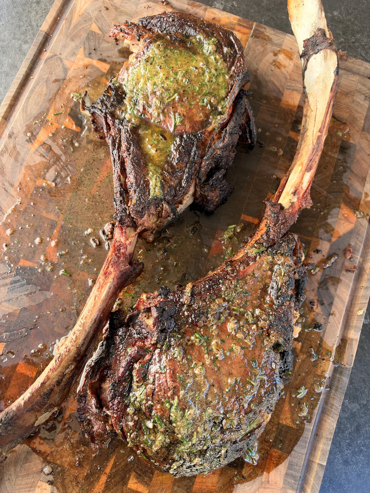 Two-bone prime rib tomahawk steaks on wooden cutting board topped with melting roasted garlic and onion compound butter
