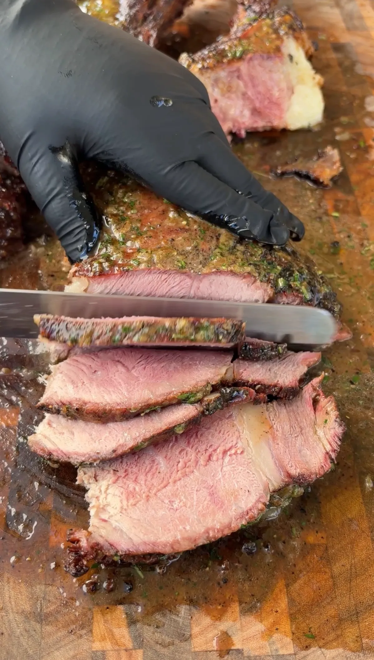 Gloved hand slicing a tomahawk prime rib against the grain with herb compound butter melting over the cuts