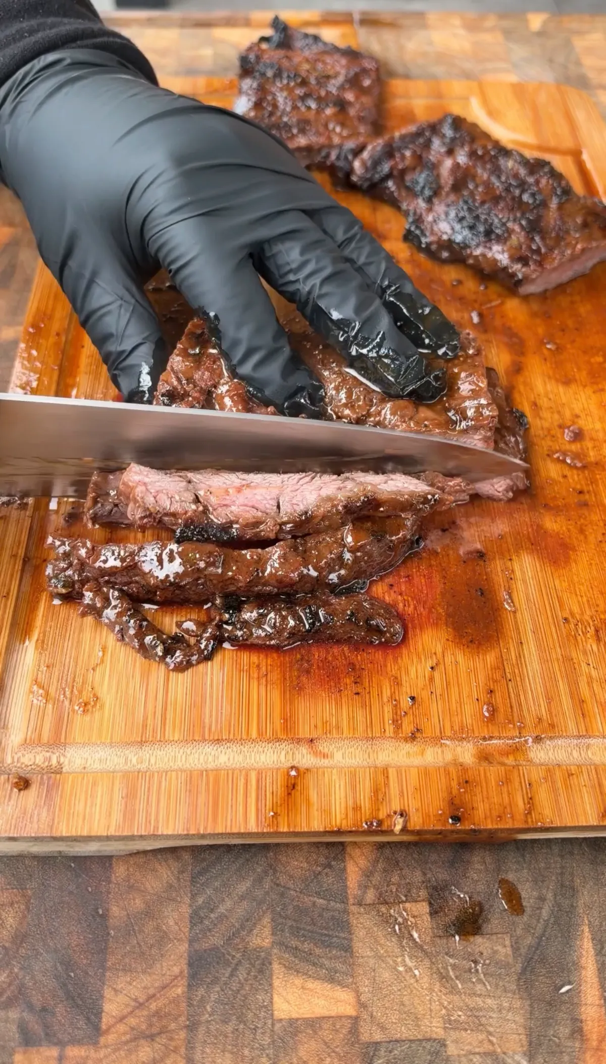 Gloved hand slicing grilled skirt steak thinly against the grain on a wooden cutting board