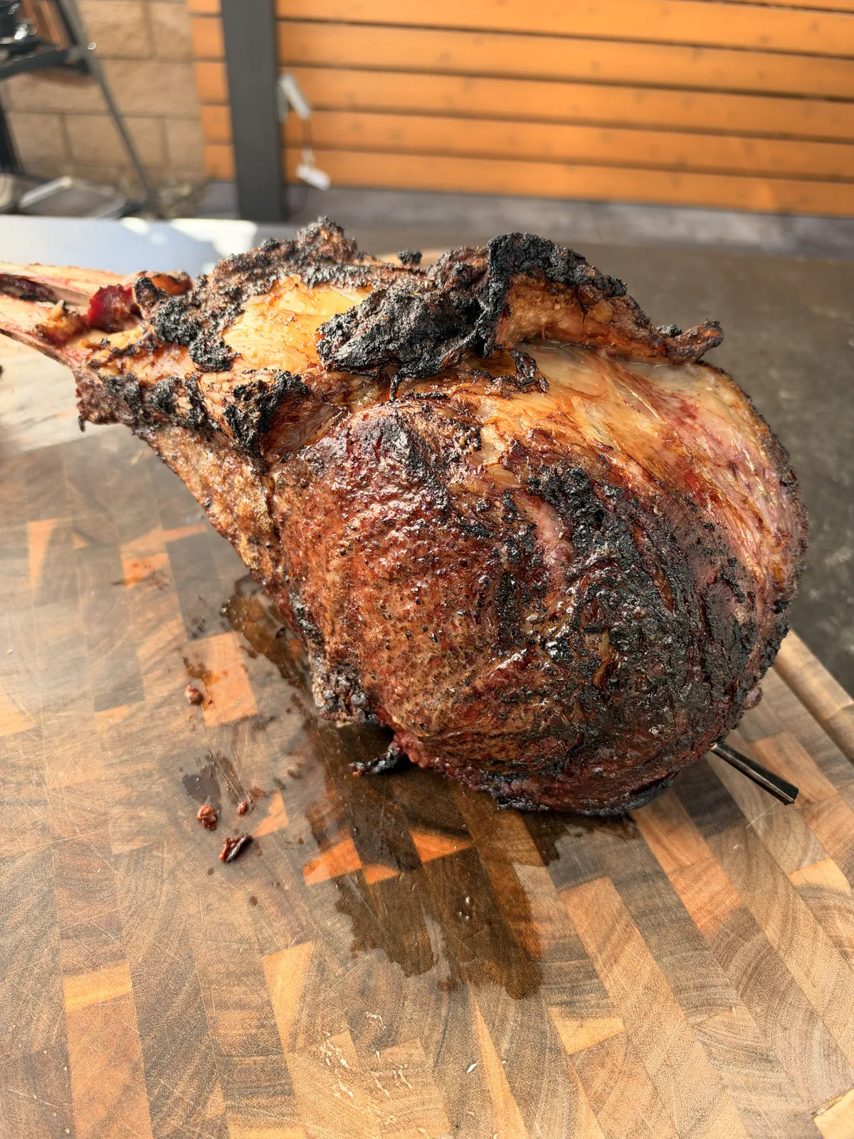 Two bone prime rib tomahawk with a deep dark crust resting on a wooden cutting board after the slow finish
