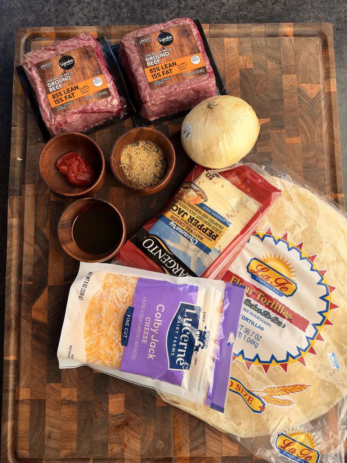Ground beef, onion, tomato paste, Worcestershire sauce, seasonings, pepper jack, Colby jack cheese, and flour tortillas on wooden board