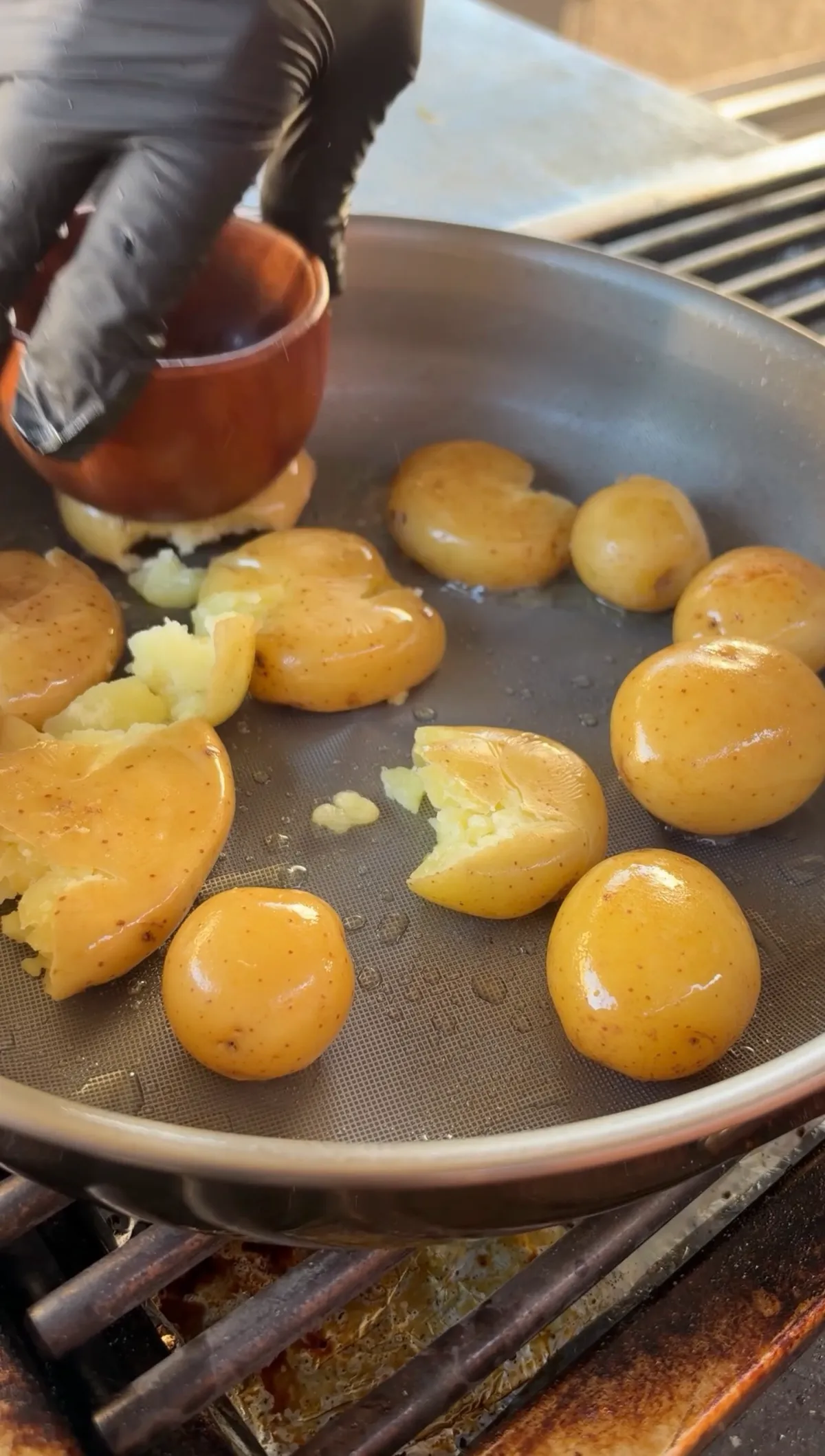 Golden potatoes being smashed with a sturdy cup in a pan, showing the crispy smashed potato step