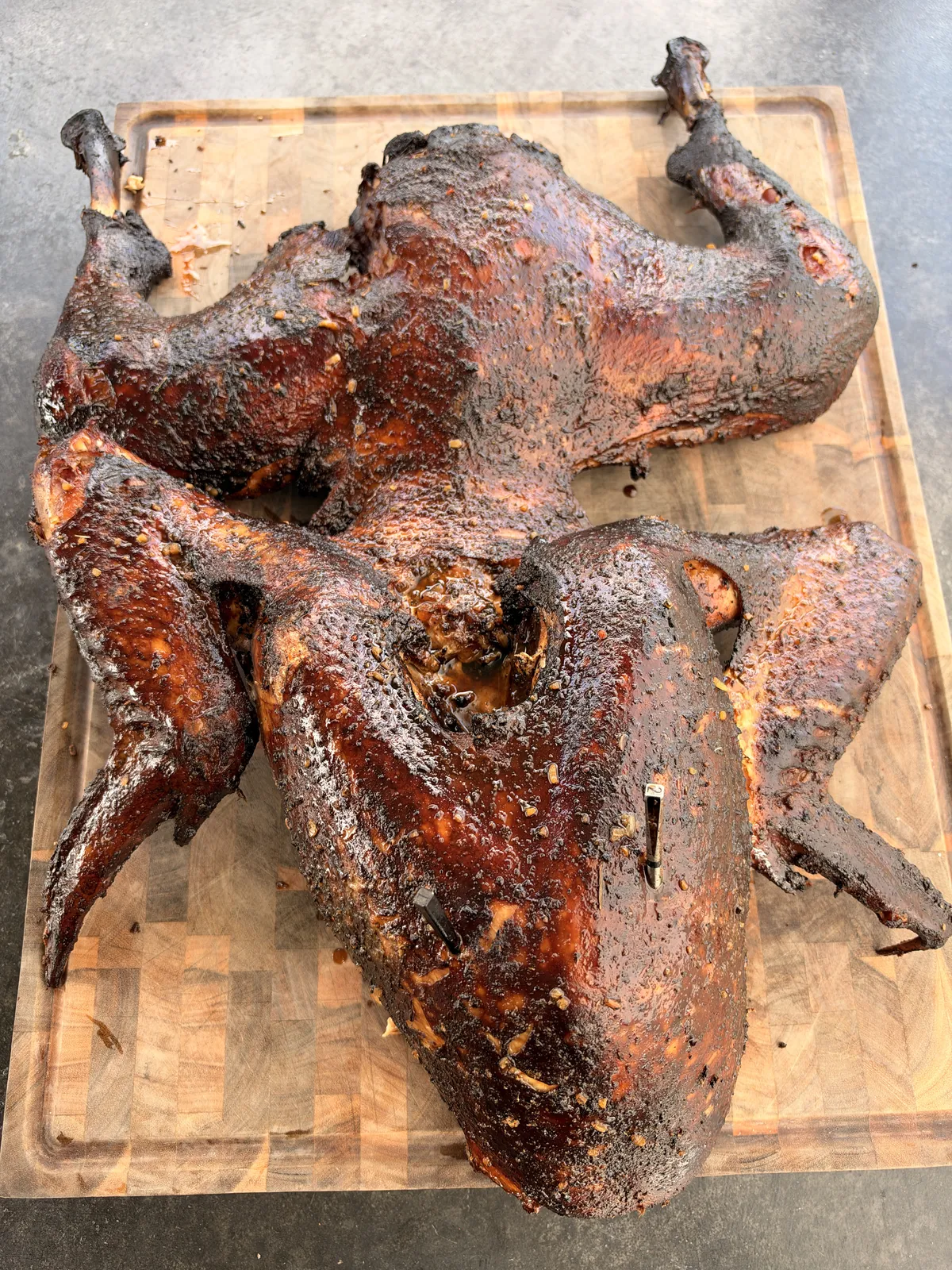 Two Cajun injected frog-style smoked turkeys with dark bark resting on a wooden cutting board