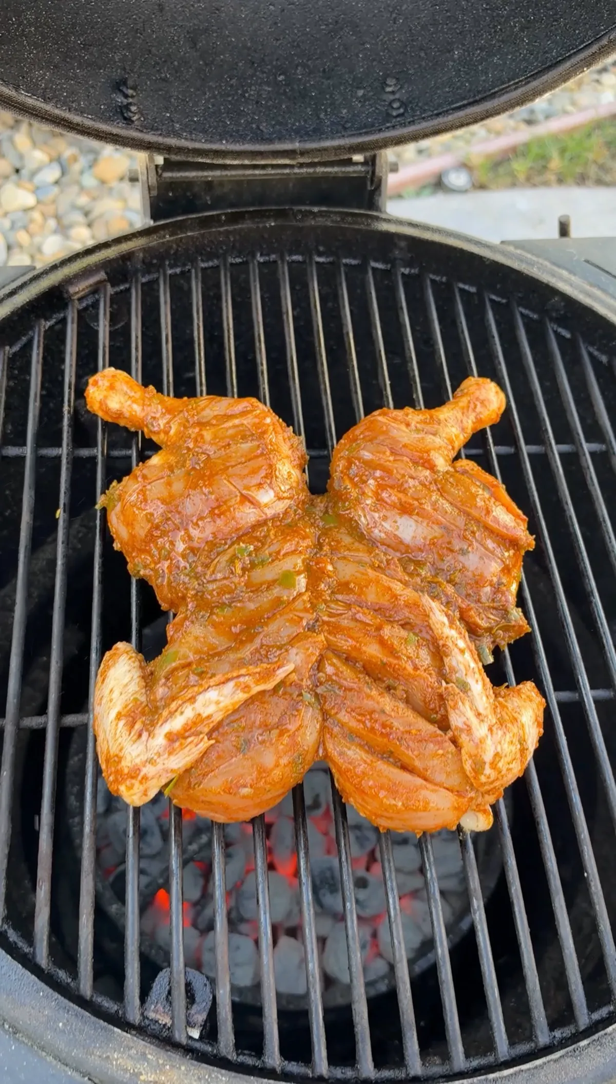 Scored spatchcocked chicken coated in green chile lime chipotle marinade grilling over hot charcoal at 350°F