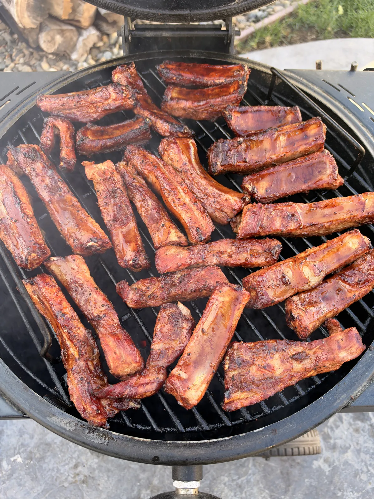 Individual St. Louis-style pork ribs smoking on round grill grates at 300–350°F, coated in cherry barbecue rub