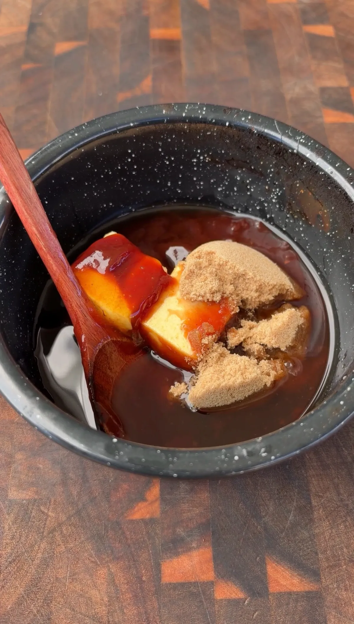 Saucepan with barbecue sauce, brown sugar, butter, and honey being stirred with a wooden spoon