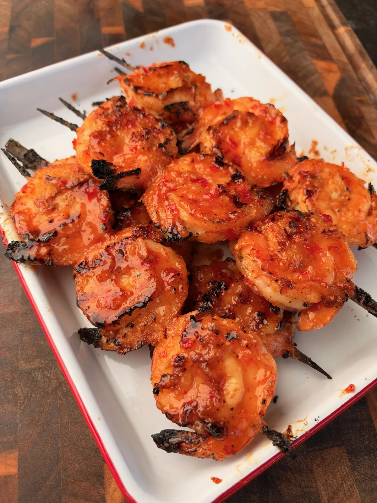 Grilled firecracker shrimp skewers coated in sticky sweet chili sriracha glaze on a white enamel platter