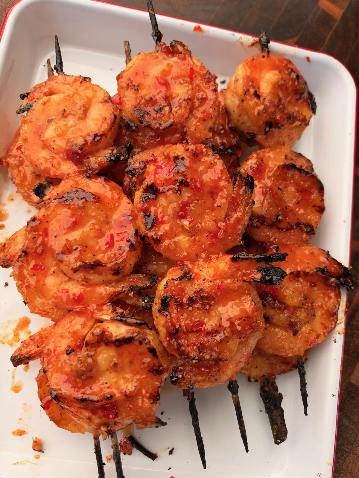 Grilled firecracker shrimp skewers coated in sticky sweet chili sriracha glaze, piled on a white rectangular platter