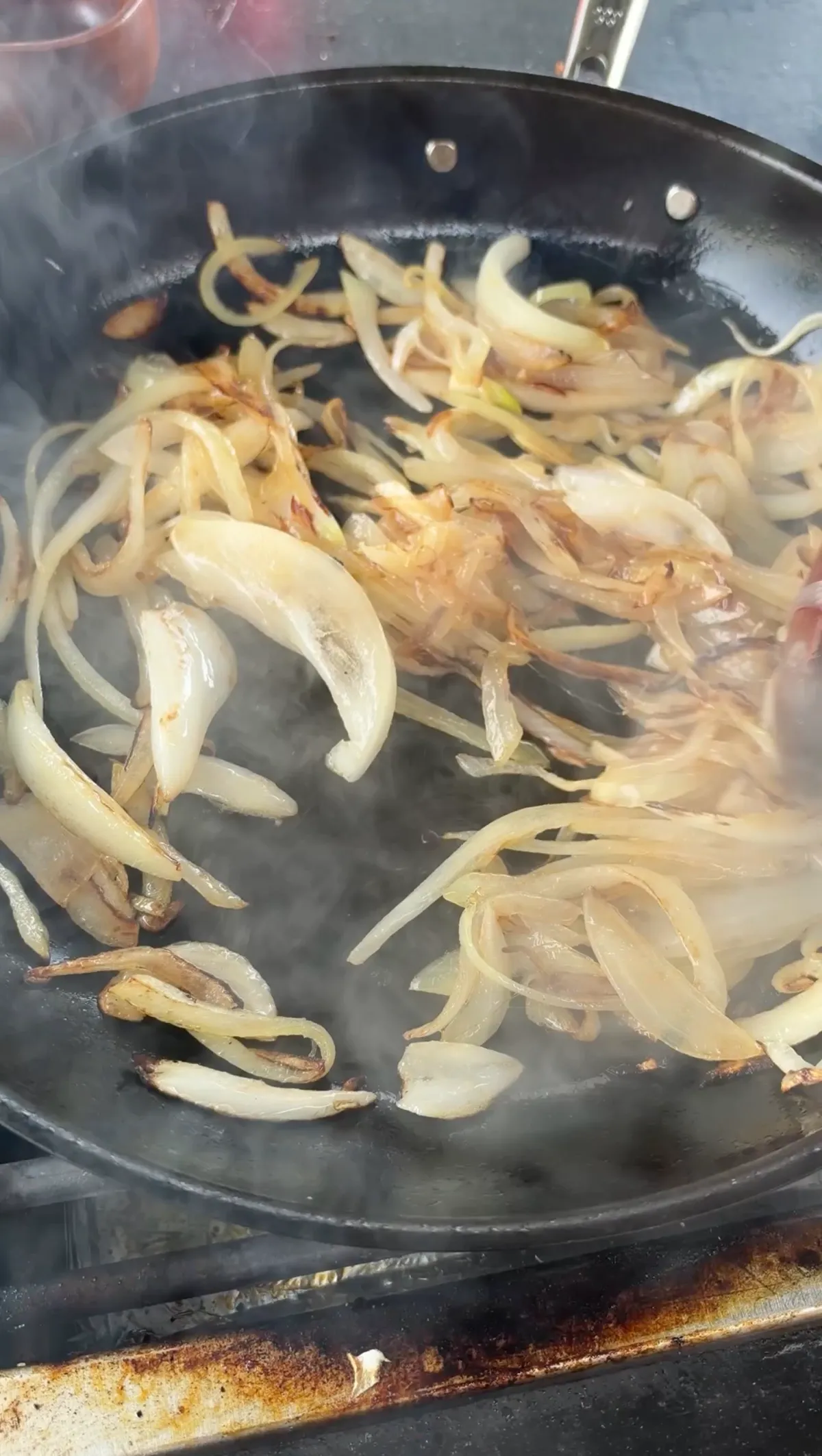 Thinly sliced sweet onions caramelizing in a black skillet, soft and golden brown for cheesesteak bread boat