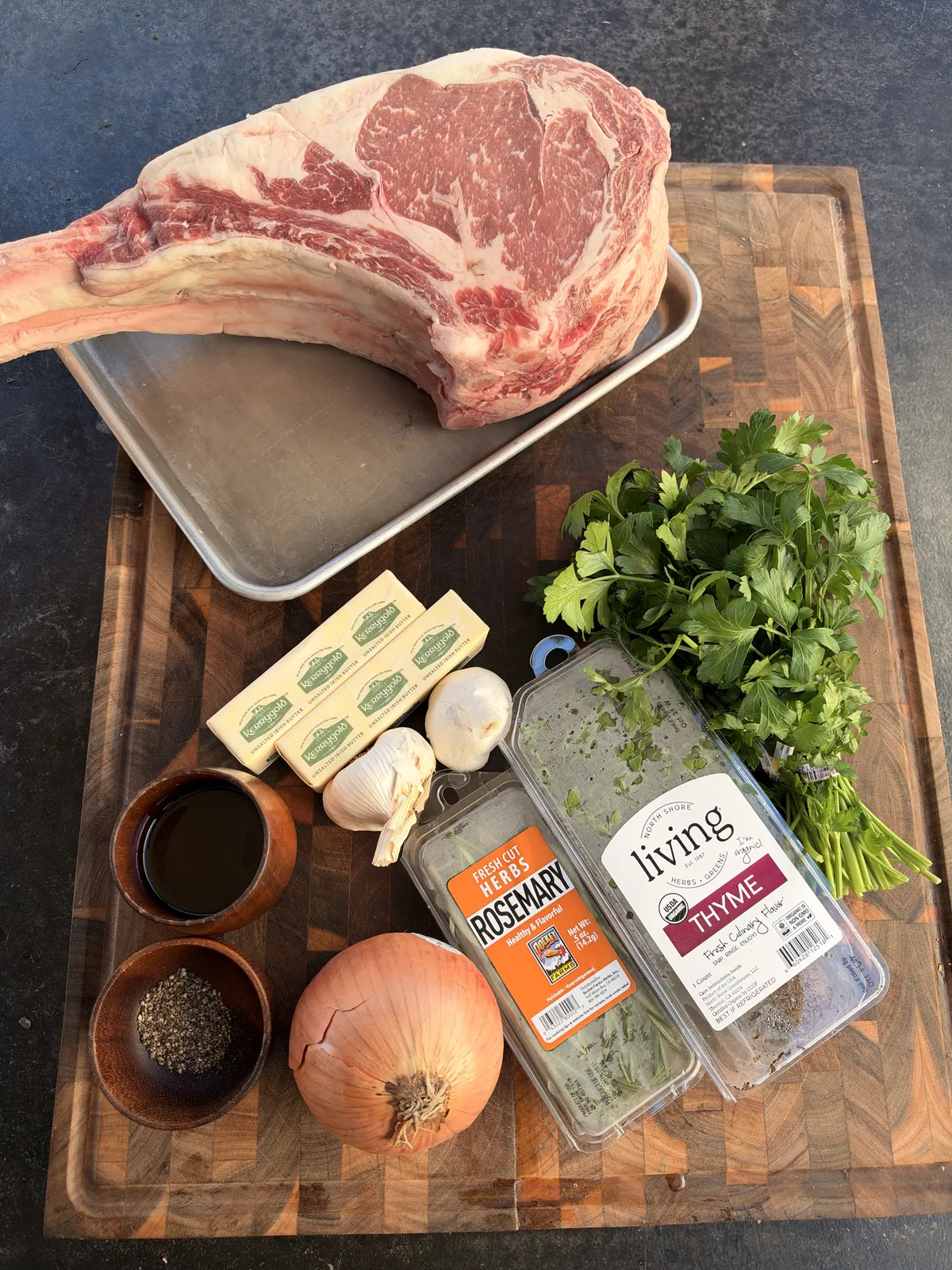 Two-bone prime rib tomahawk with compound butter ingredients: Kerrygold butter, garlic, white onion, rosemary, thyme, parsley, soy sauce, and black pepper