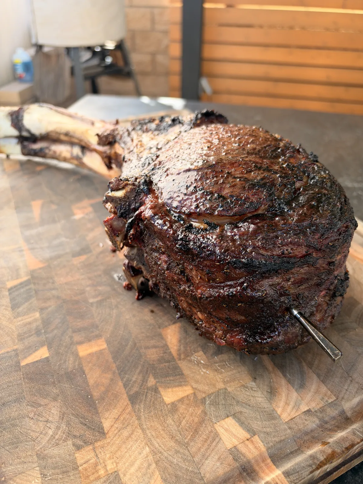 Two-bone prime rib tomahawk with deep seared crust and meat thermometer on end-grain cutting board